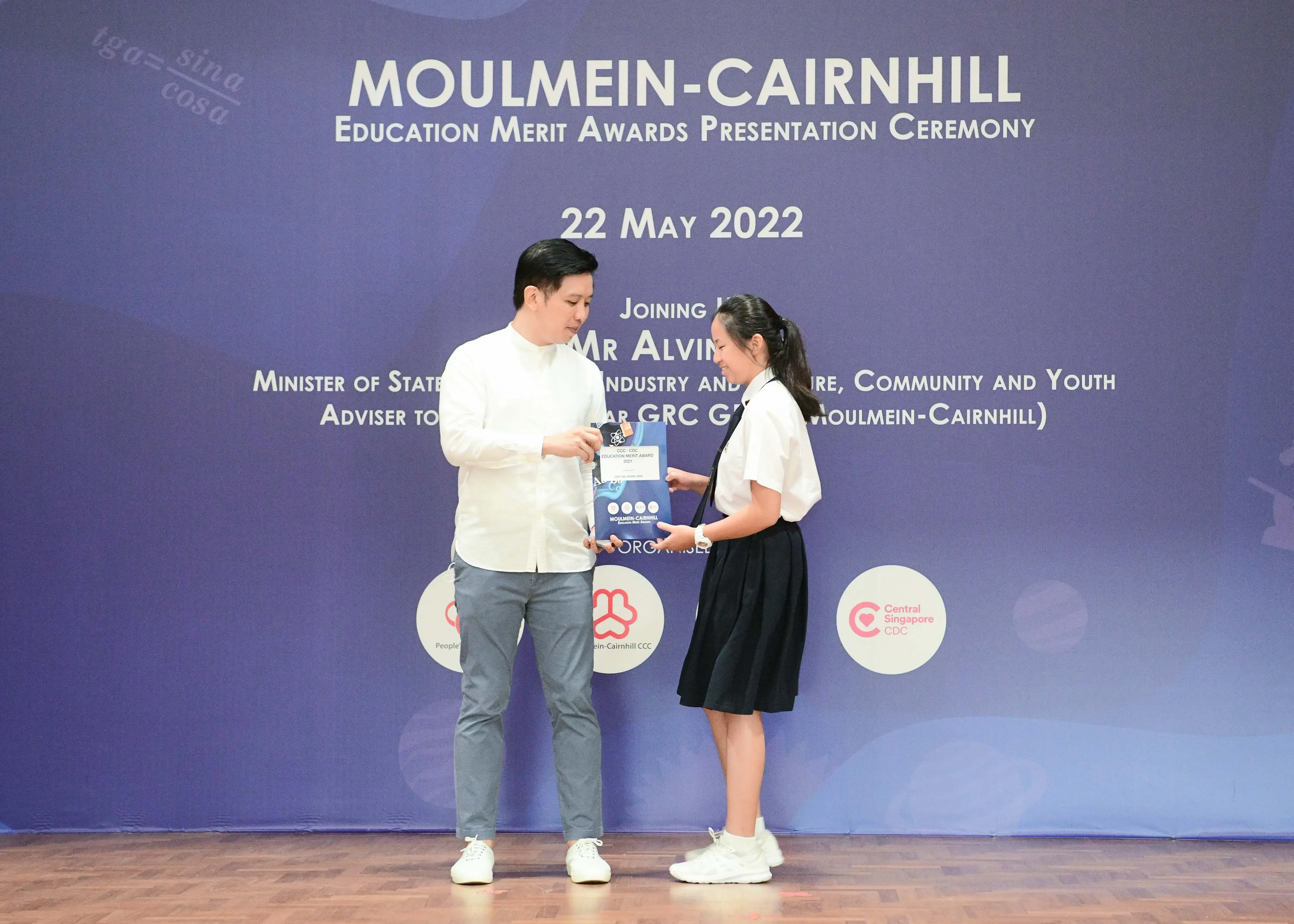 A man in white shirt hands an award to a young girl in school uniform at the Moulmein-Cairnhill Education Merit Awards 2022.