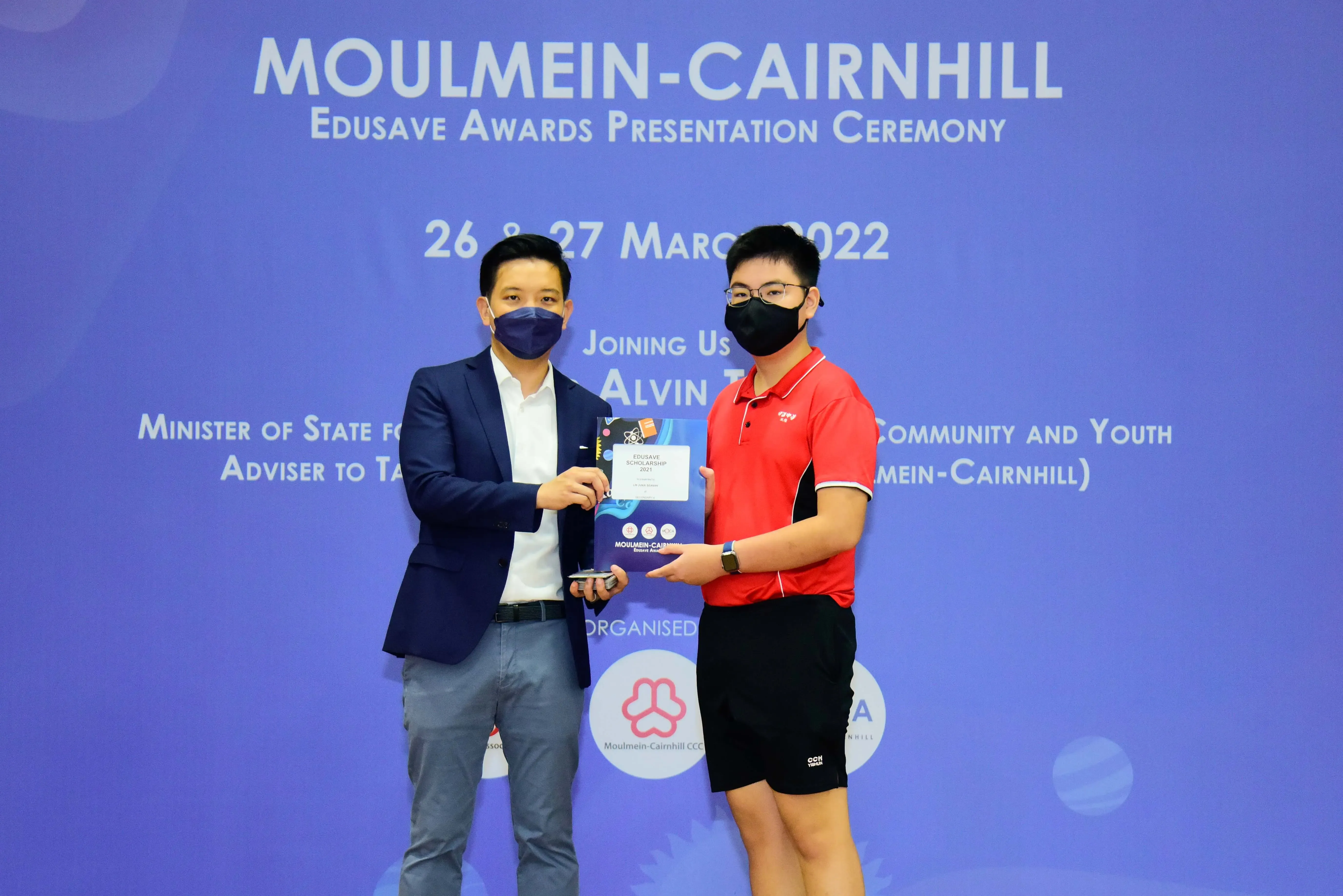 Two masked individuals hold an Edusave Scholarship certificate at the Moulmein-Cairnhill Awards Ceremony, March 2022.