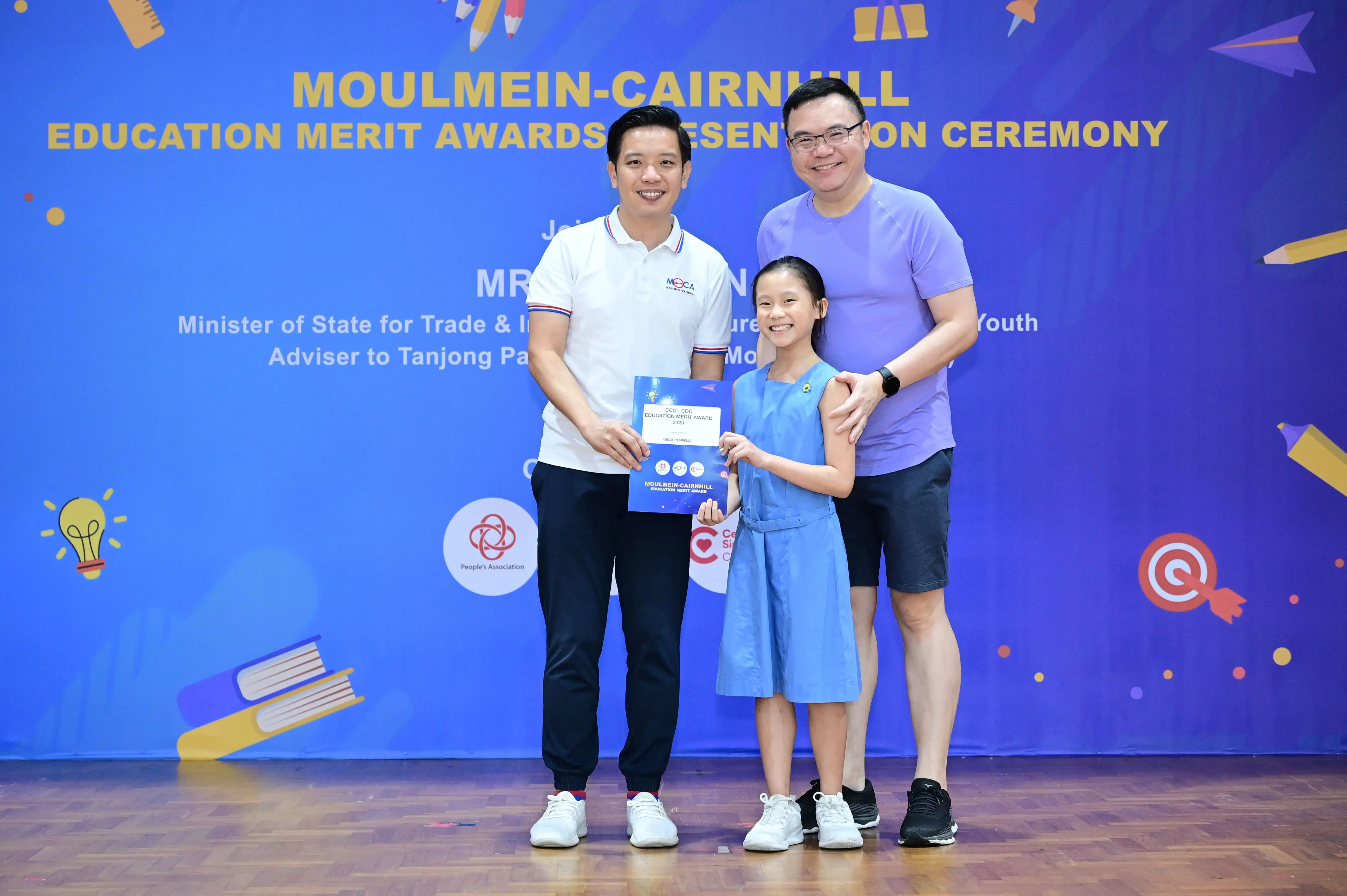Two men and a girl holding a certificate at the Moulmein-Cairnhill Education Merit Awards Presentation Ceremony.