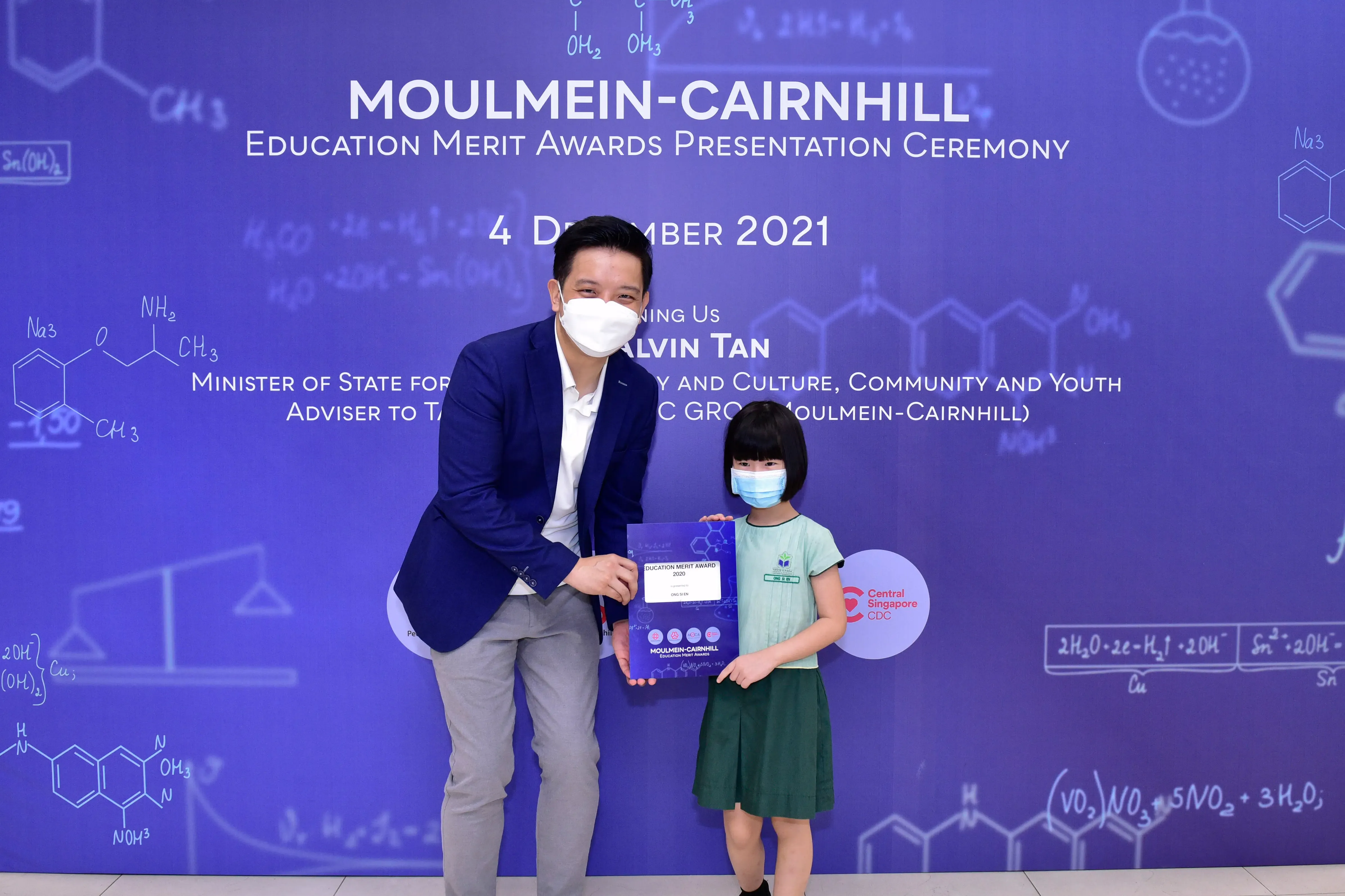 A man and a young girl wearing masks hold an award certificate at the Moulmein-Cairnhill Education Merit Awards 2021.