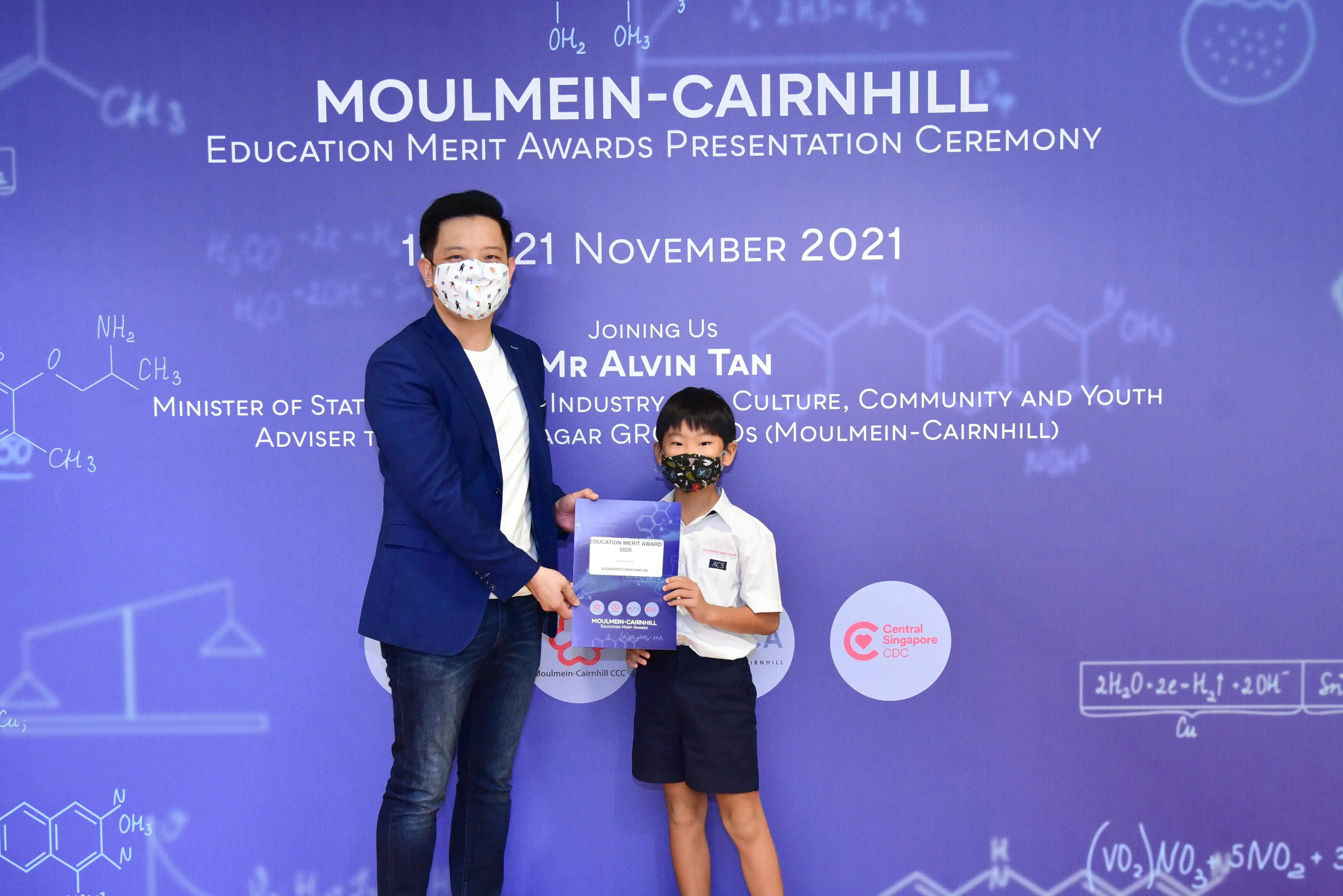 A man and a young boy in masks hold an award certificate at the Moulmein-Cairnhill Education Merit Awards 2021.