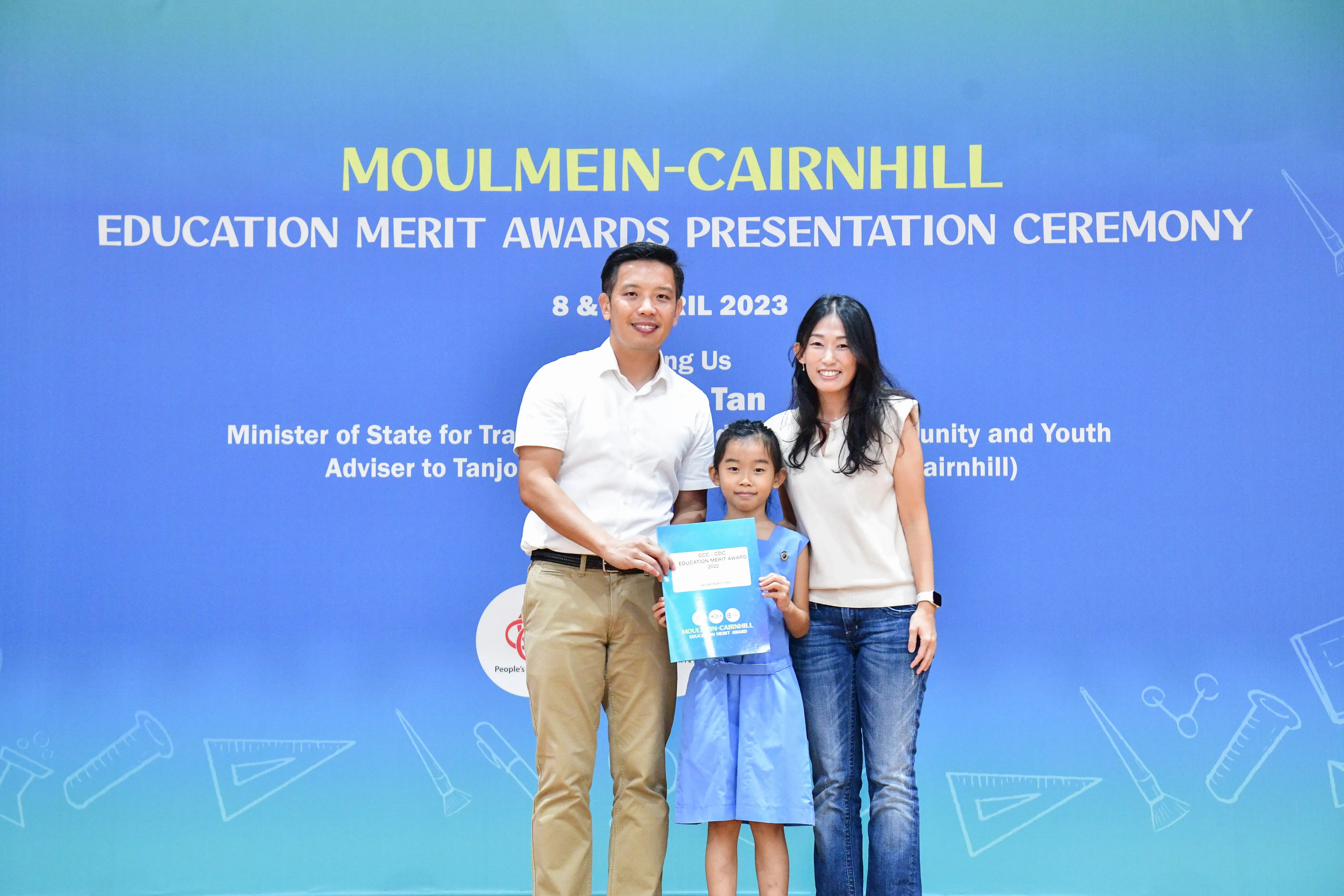 A man and woman stand with a young girl holding an award at the Moulmein-Cairnhill Education Merit Awards 2023.