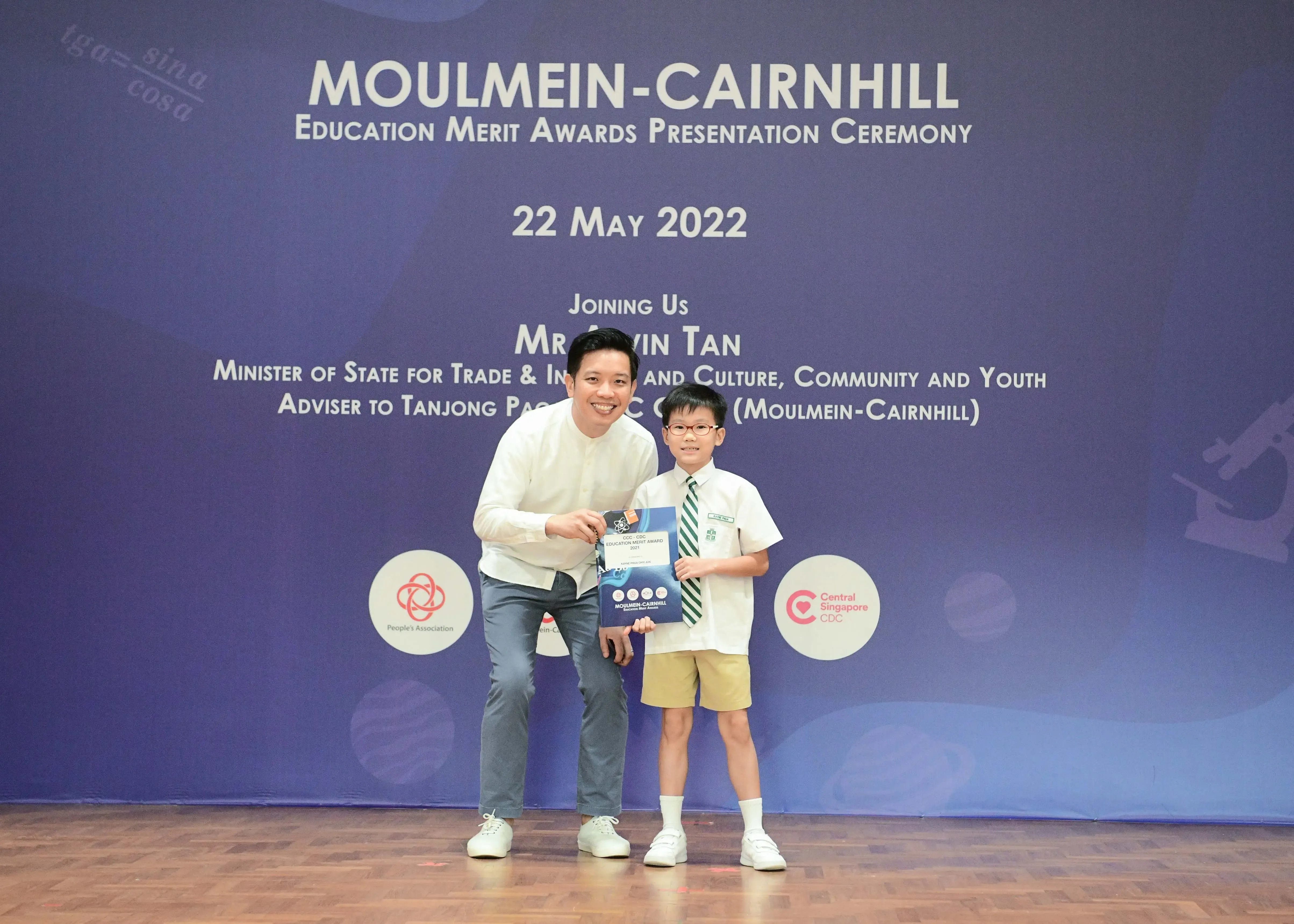 A man and a young boy in school uniform pose together holding an award at the Moulmein-Cairnhill Education Merit Awards ceremony.