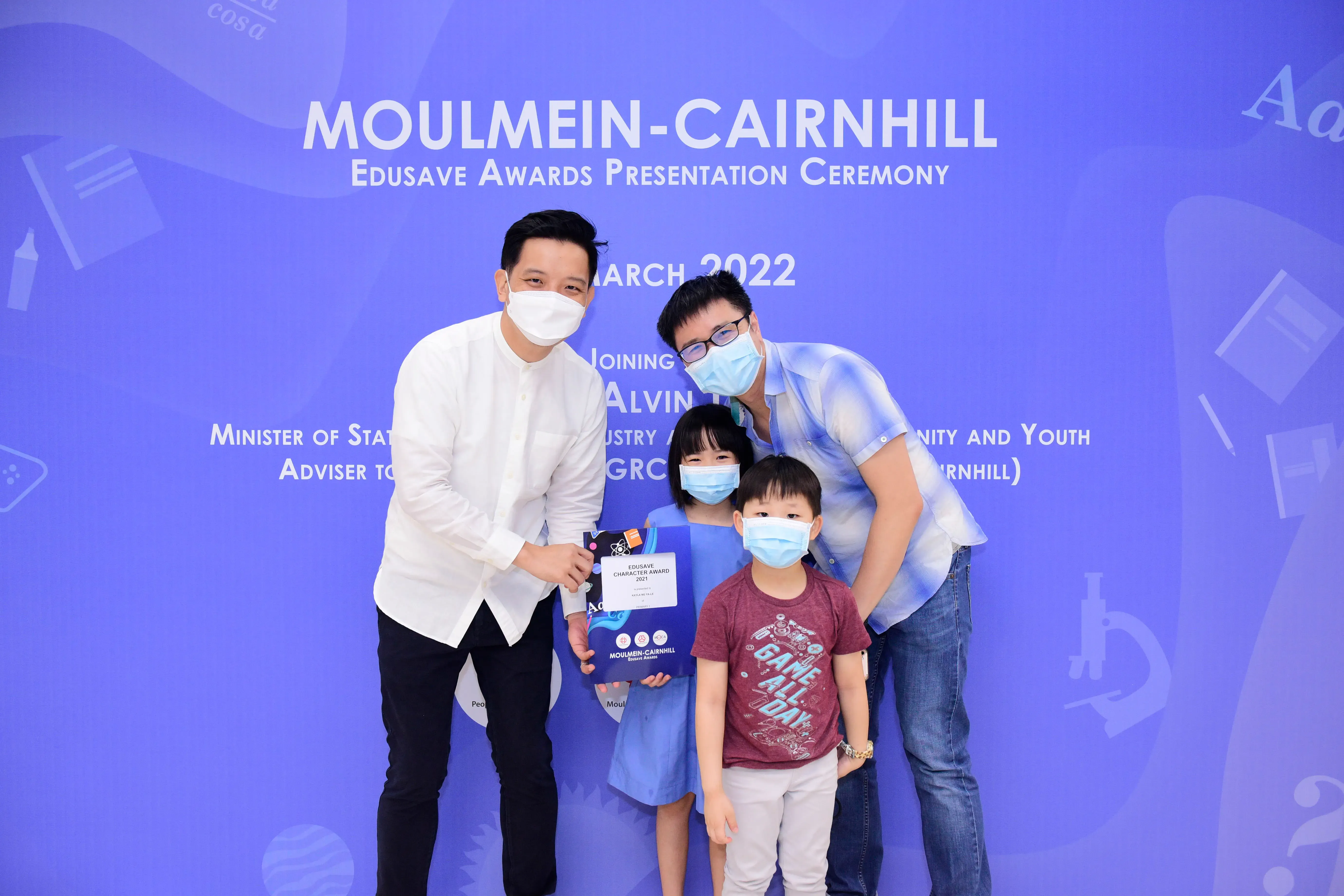 Four masked people pose at the Moulmein-Cairnhill Edusave Awards Ceremony in March 2022, holding an award certificate.