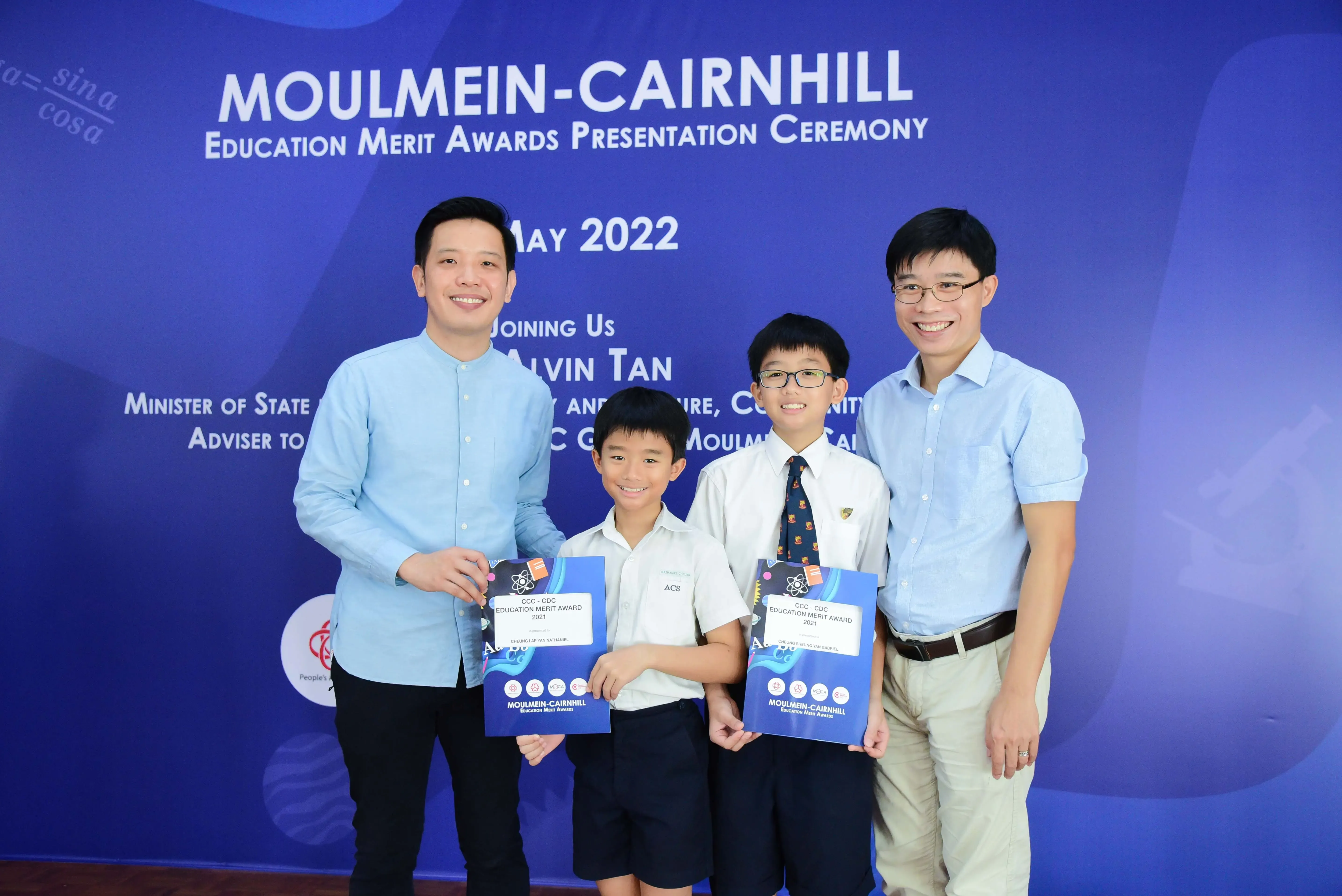 Two men and two boys pose smiling at the Moulmein-Cairnhill Education Merit Awards ceremony, May 2022.