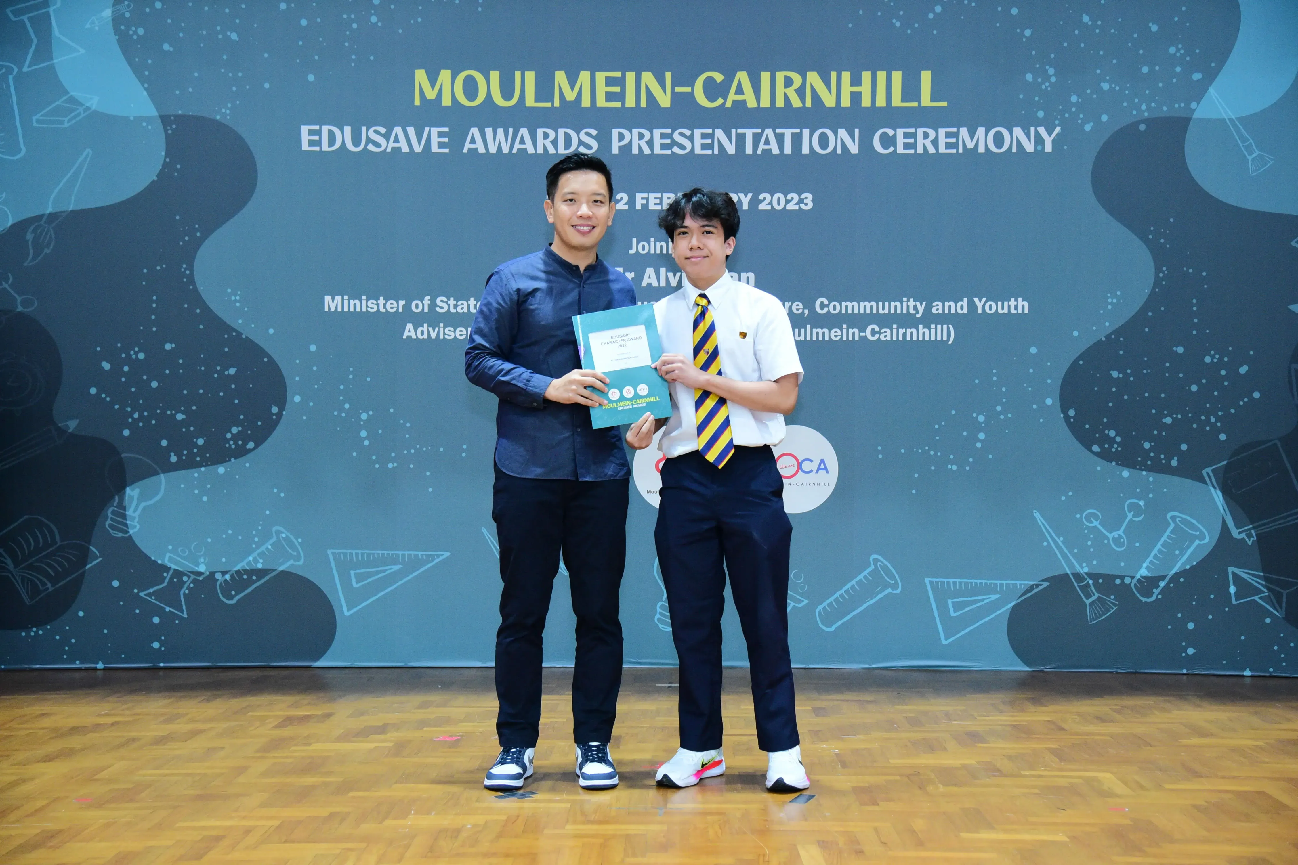 Two men hold a certificate together at the Moulmein-Cairnhill Edusave Awards Presentation Ceremony in 2023.