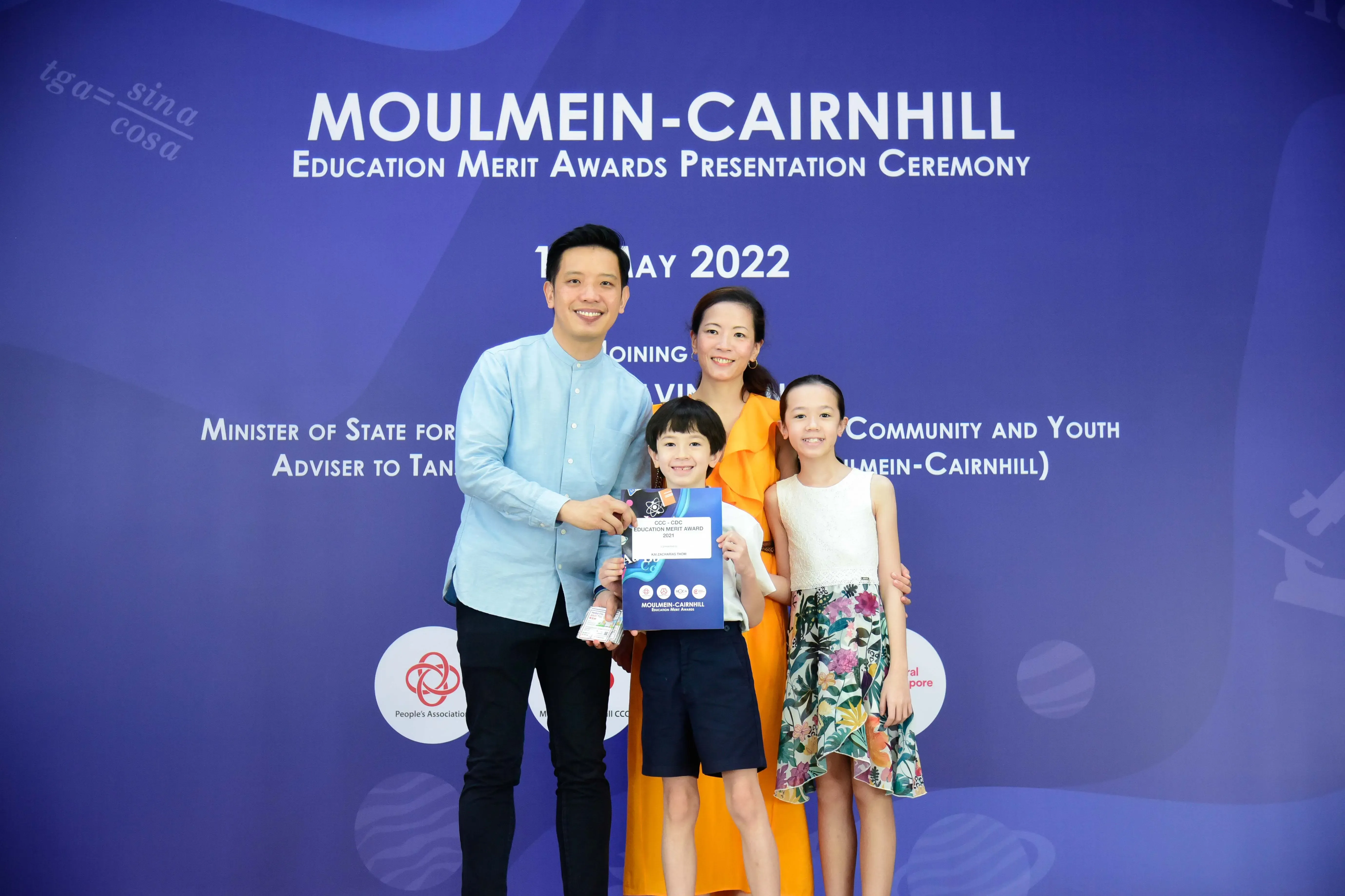 Two adults and two children pose with an award certificate at the Moulmein-Cairnhill Education Merit Awards ceremony, May 2022.
