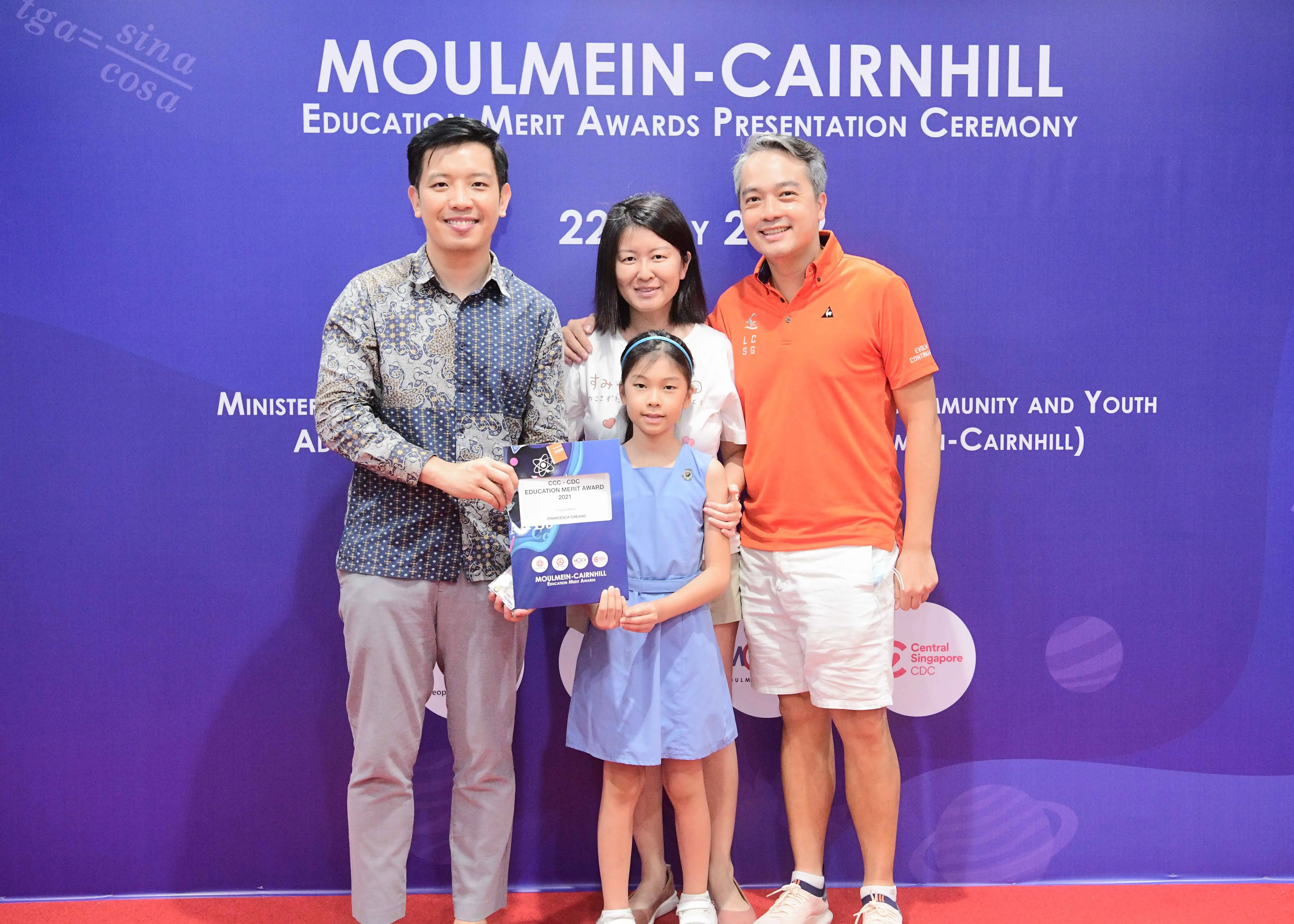 Three adults and a girl holding an award certificate at the Moulmein-Cairnhill Education Merit Awards ceremony.