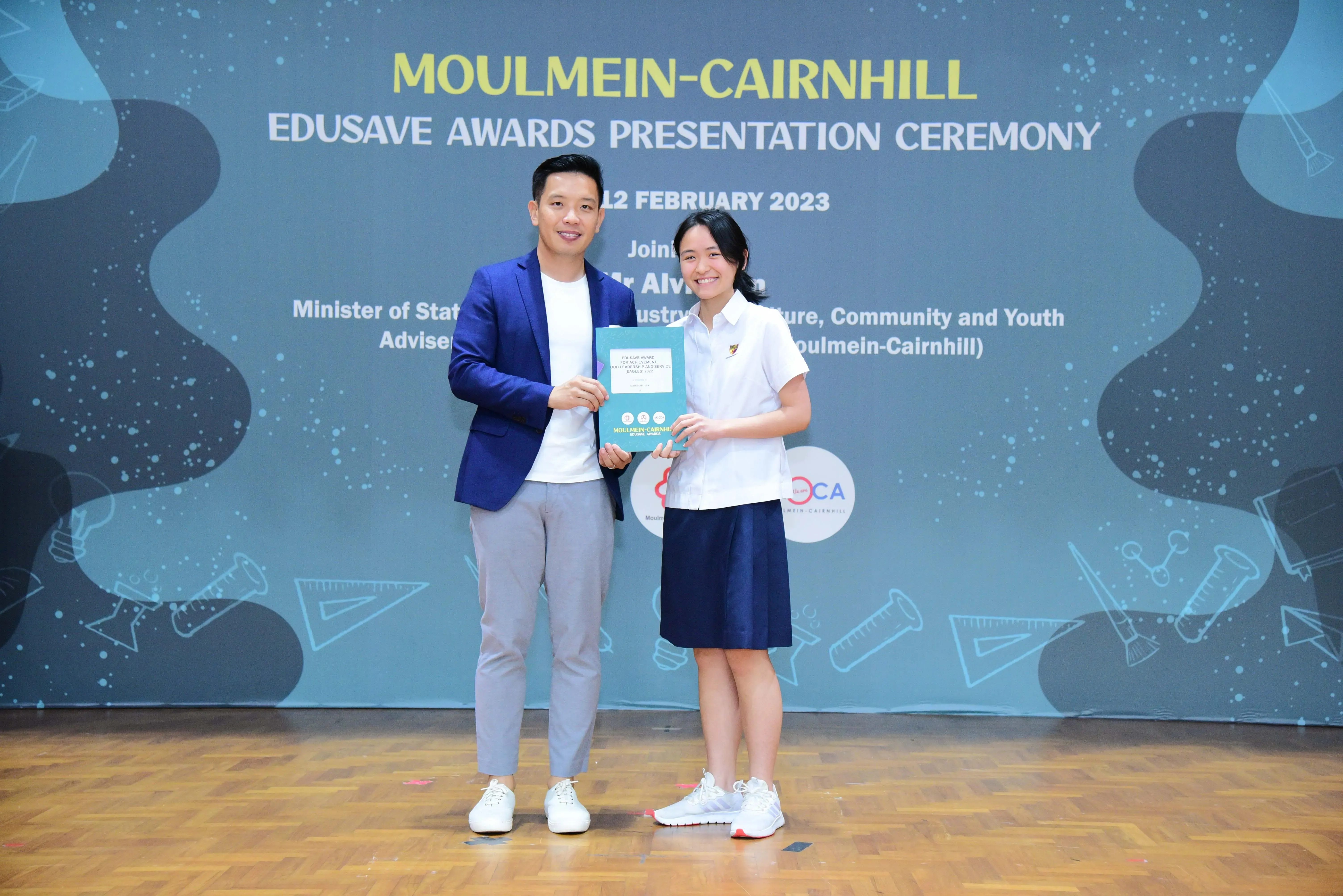 Two people hold an award booklet on stage at the Moulmein-Cairnhill Edusave Awards Presentation Ceremony, February 2023.
