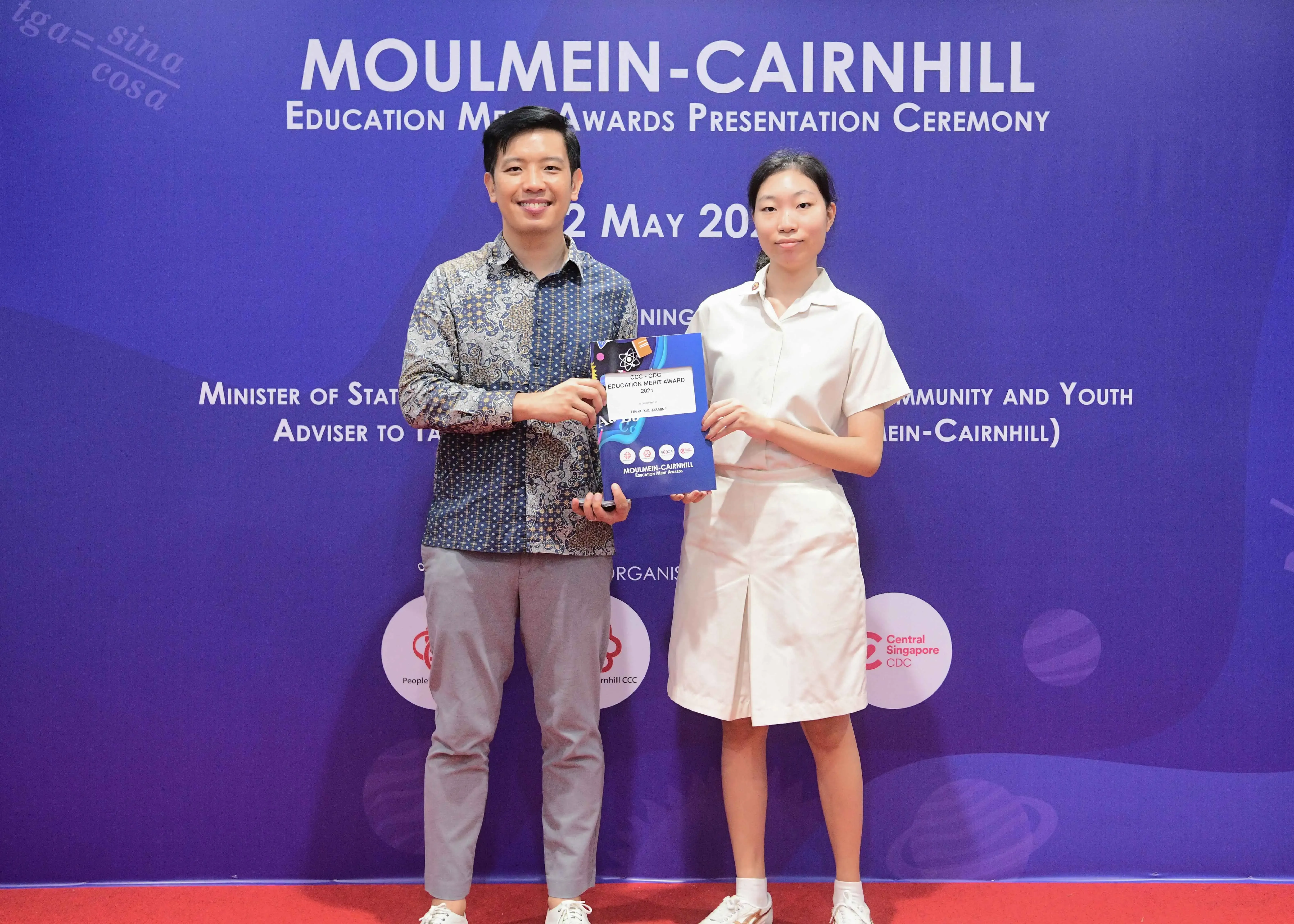 Two people hold an award certificate at the Moulmein-Cairnhill Education Merit Awards Presentation Ceremony.