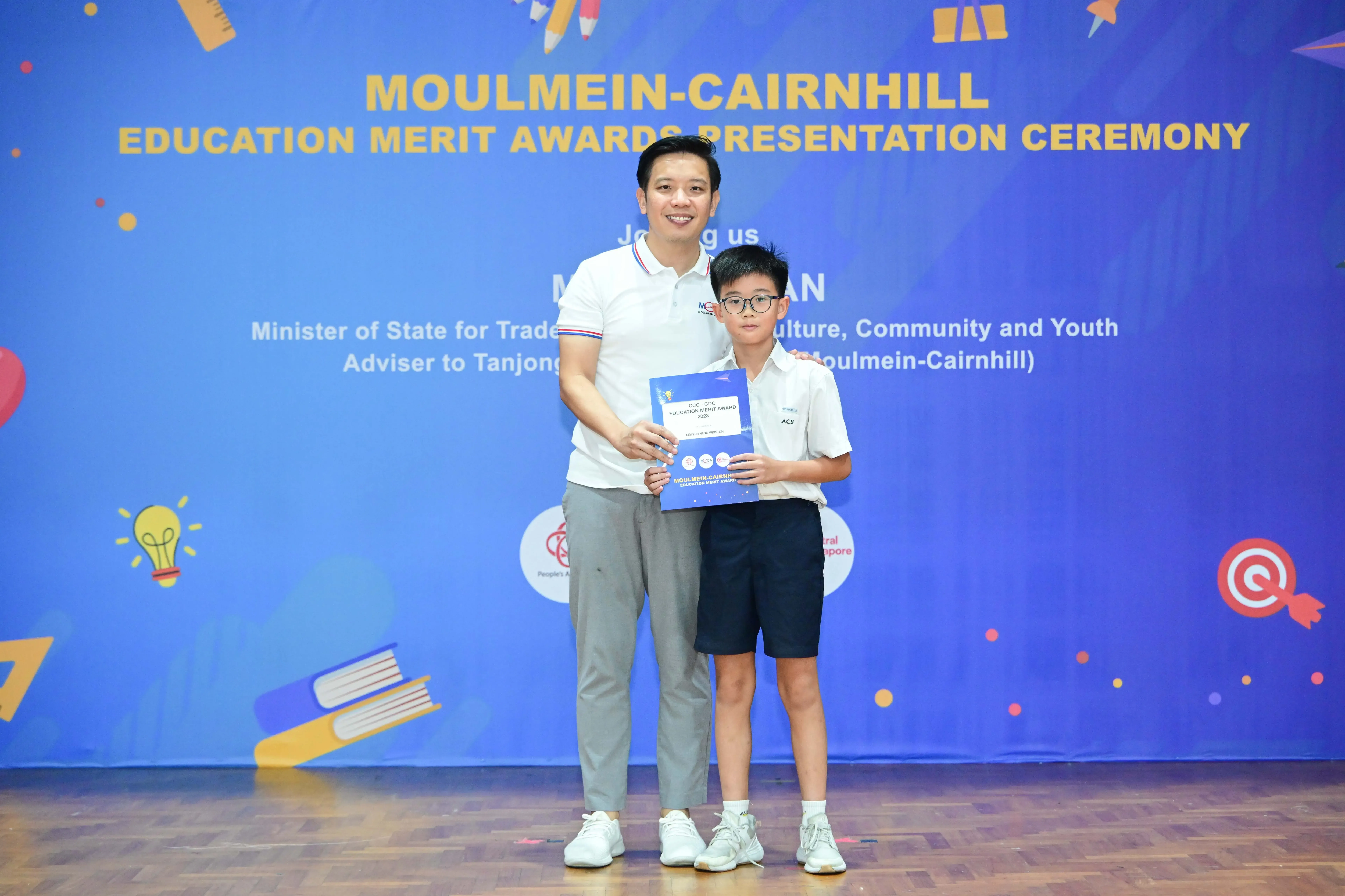 A man and a young boy hold a certificate together at the Moulmein-Cairnhill Education Merit Awards Presentation Ceremony.