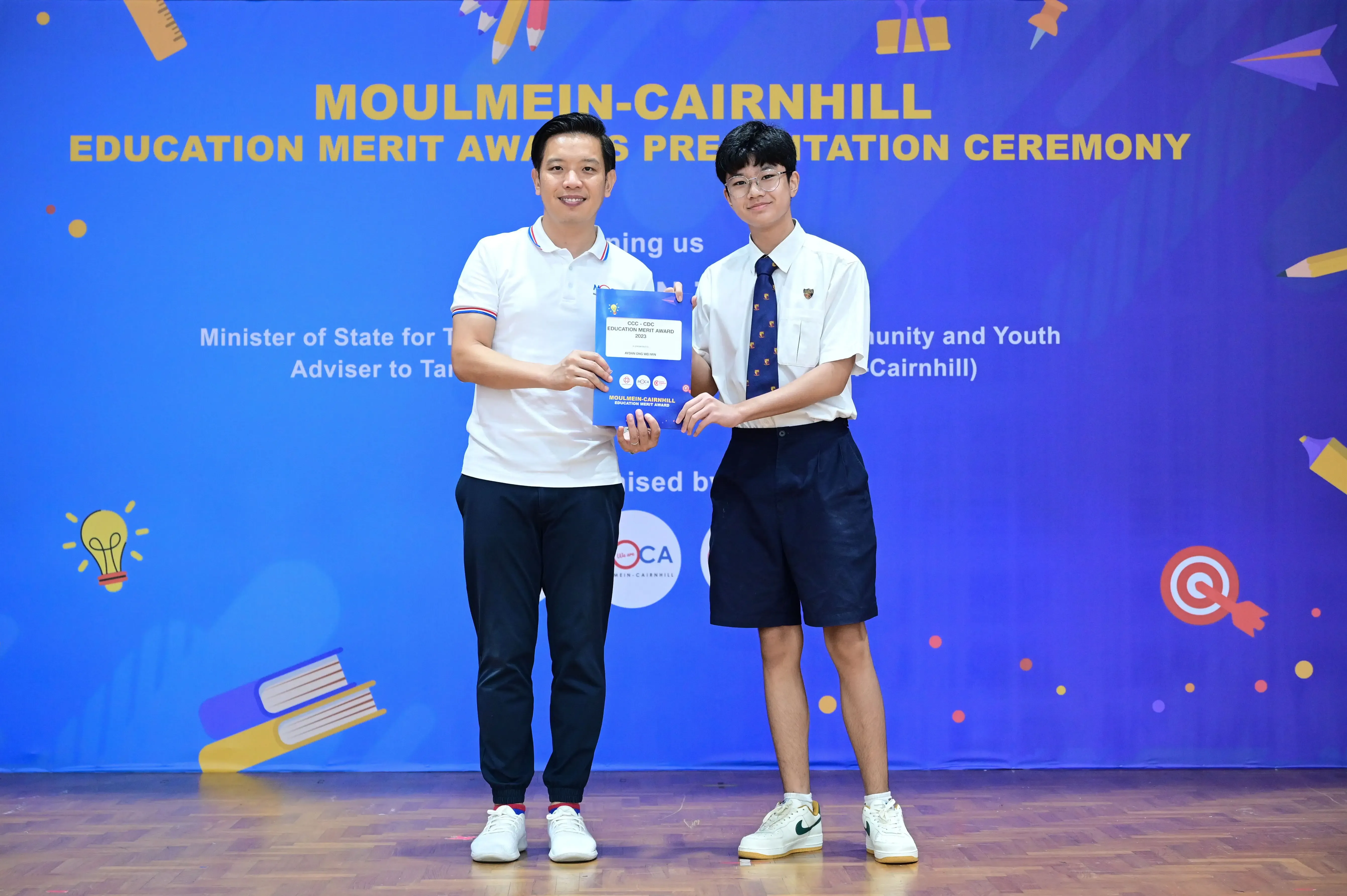 Two people hold an award certificate at the Moulmein-Cairnhill Education Merit Awards Presentation Ceremony.