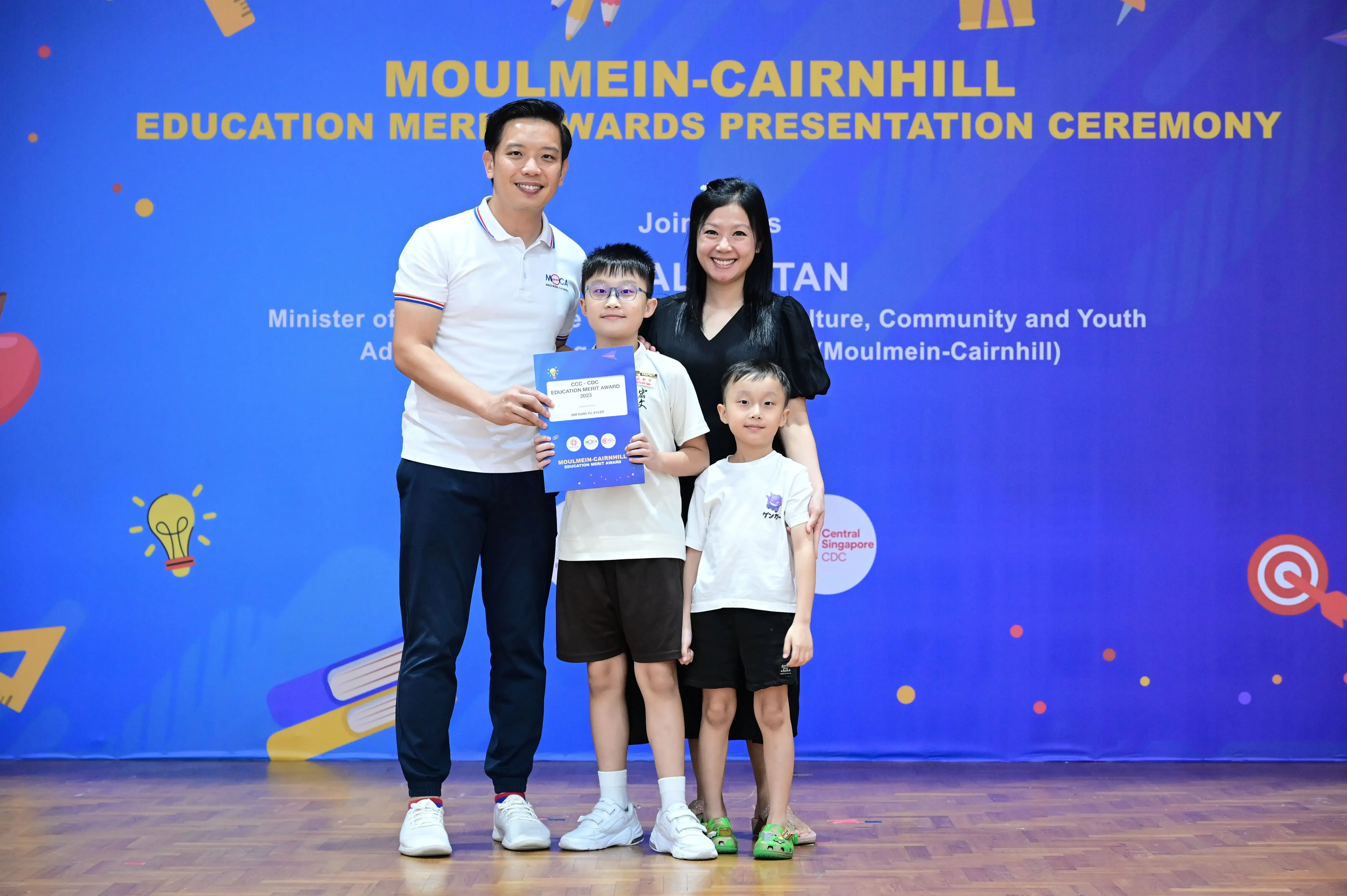 Two adults and two children pose with a certificate at the Moulmein-Cairnhill Education Merit Awards Ceremony.