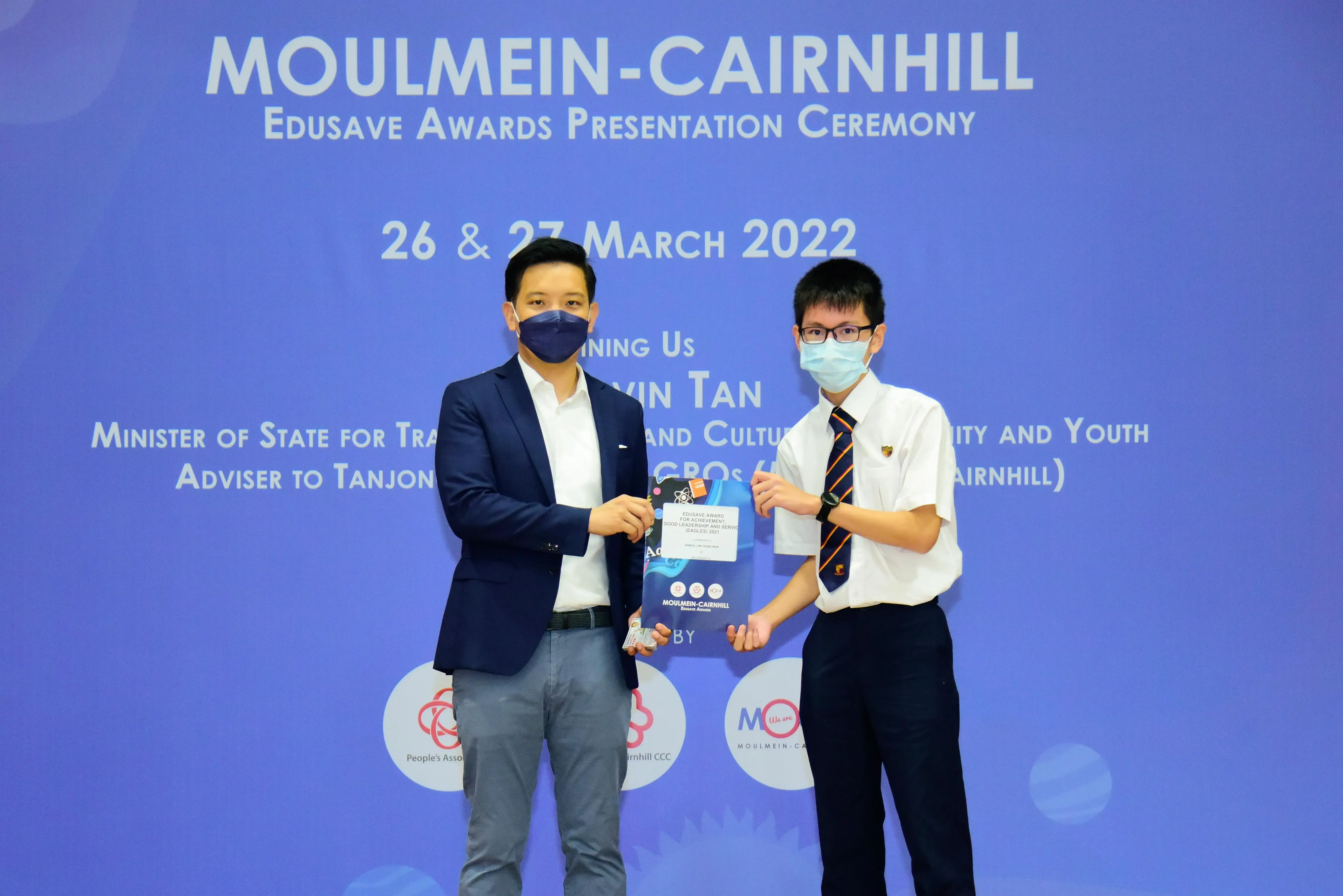 Two masked individuals hold an award at the Moulmein-Cairnhill Edusave Awards Presentation Ceremony, March 2022.