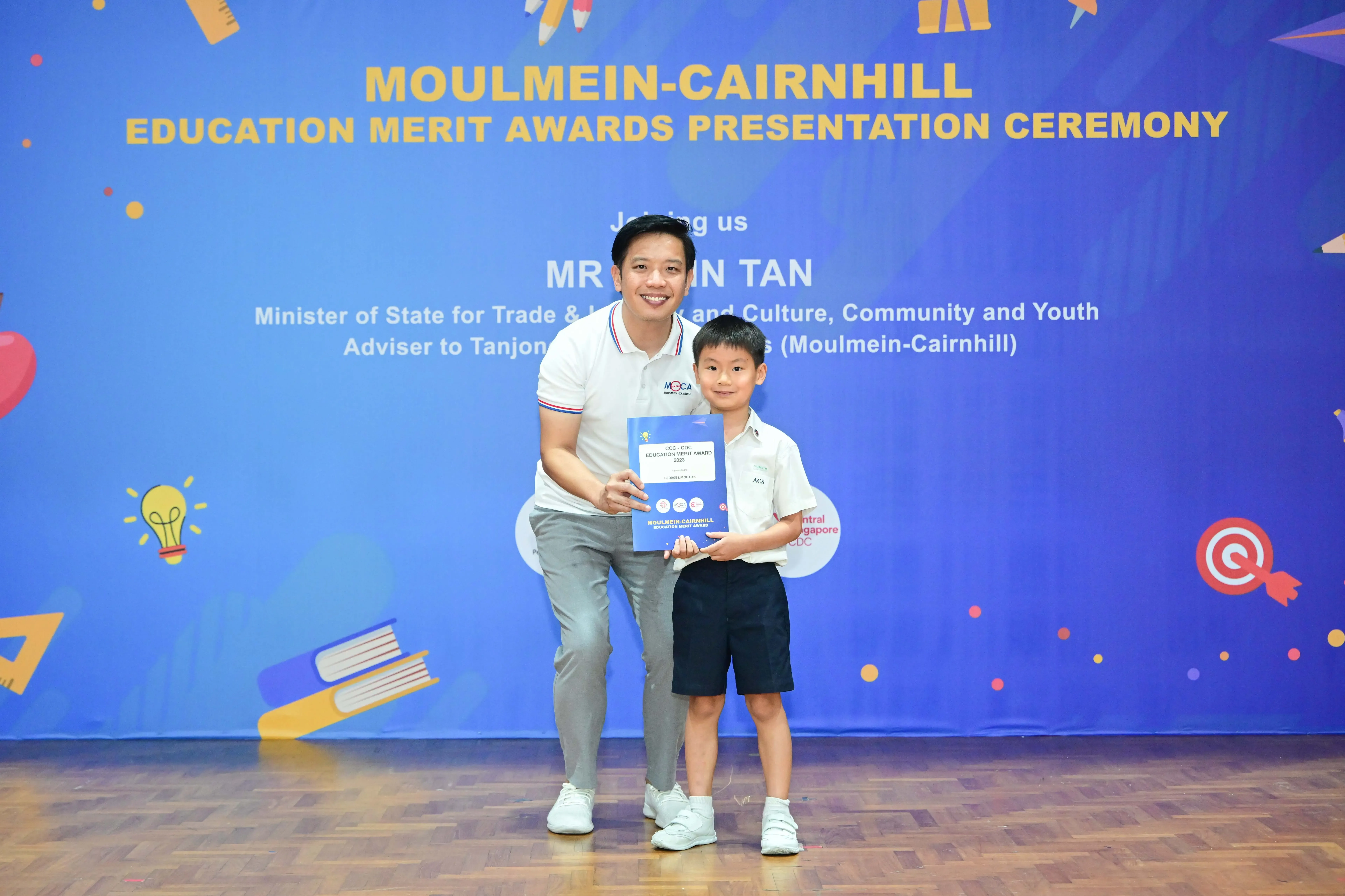 Man and young boy holding a blue award booklet at Moulmein-Cairnhill Education Merit Awards Presentation Ceremony.