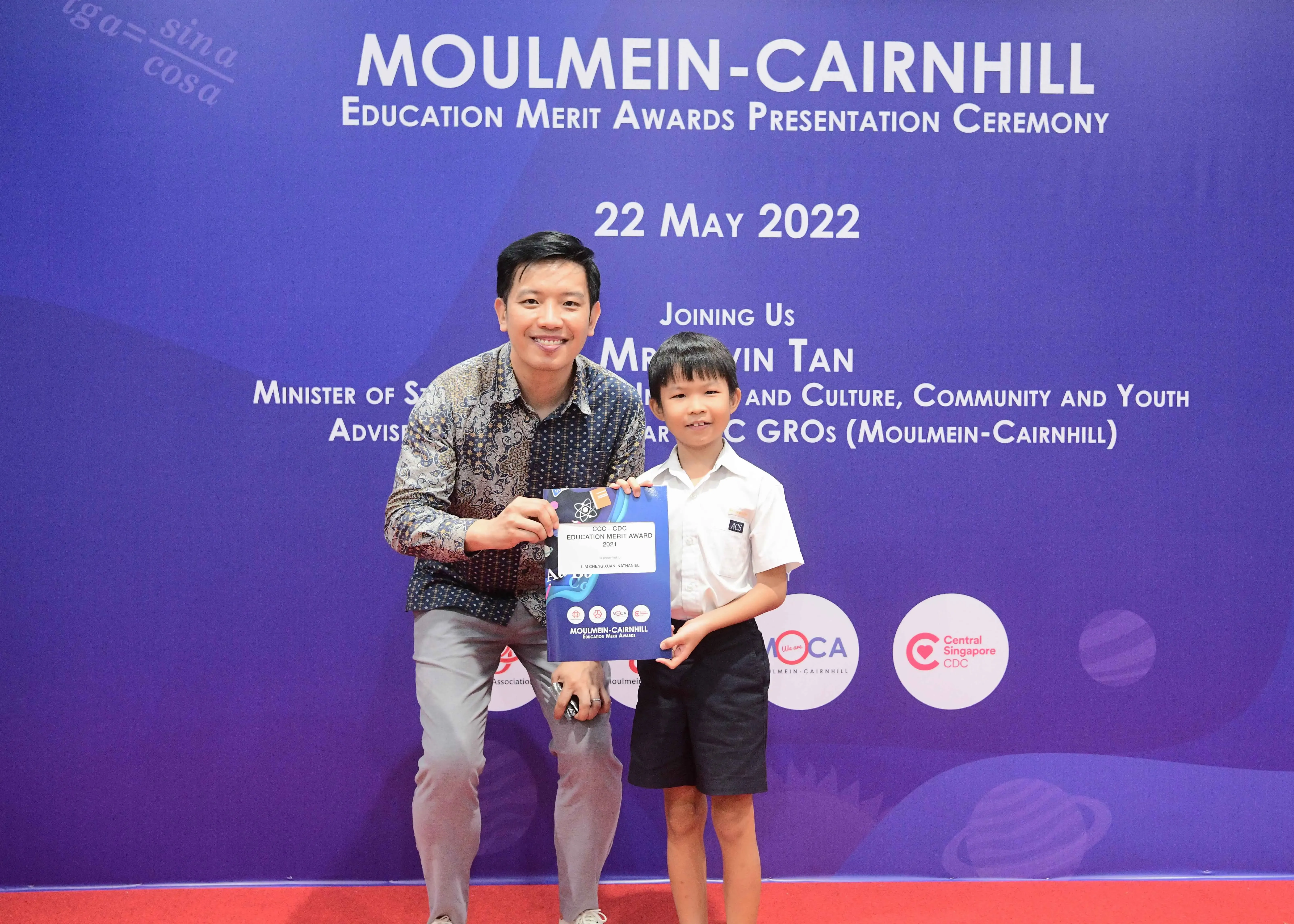 A man and a young boy hold an award certificate at the Moulmein-Cairnhill Education Merit Awards ceremony on 22 May 2022.