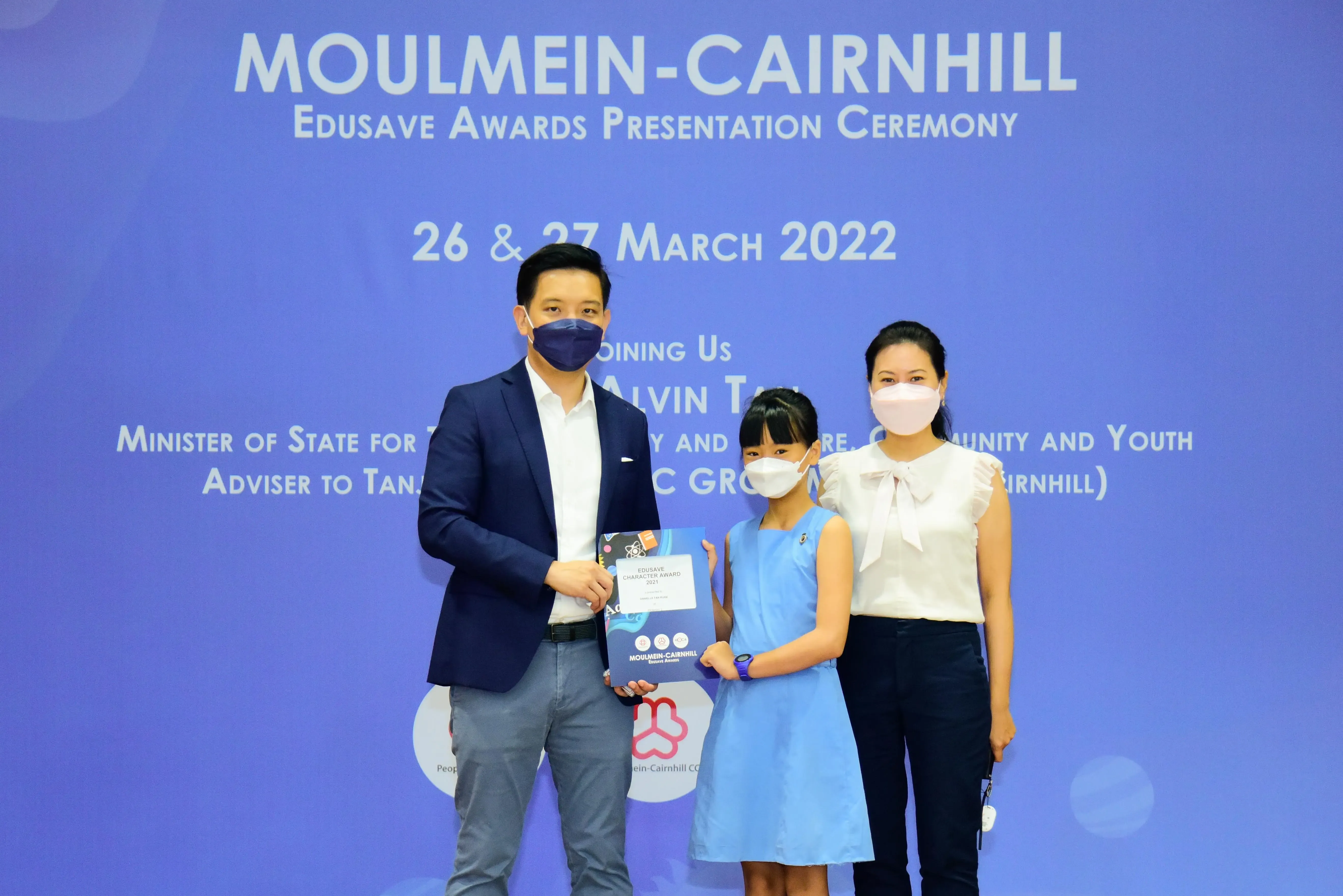 Two adults and a child in masks pose with an award certificate at the Moulmein-Cairnhill Edusave Awards Ceremony 2022.