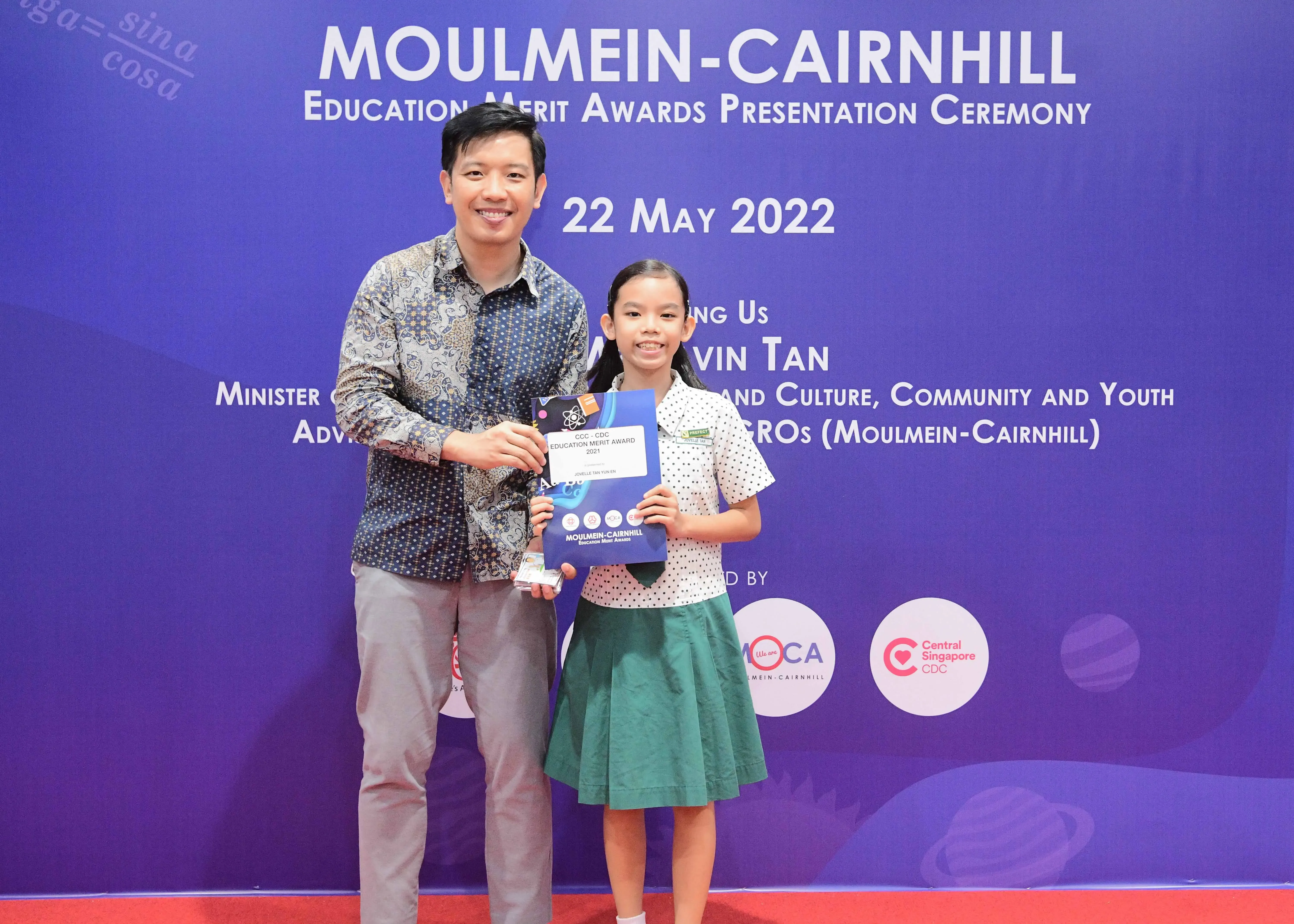 Man and young girl pose holding an award certificate at the Moulmein-Cairnhill Education Merit Awards on 22 May 2022.