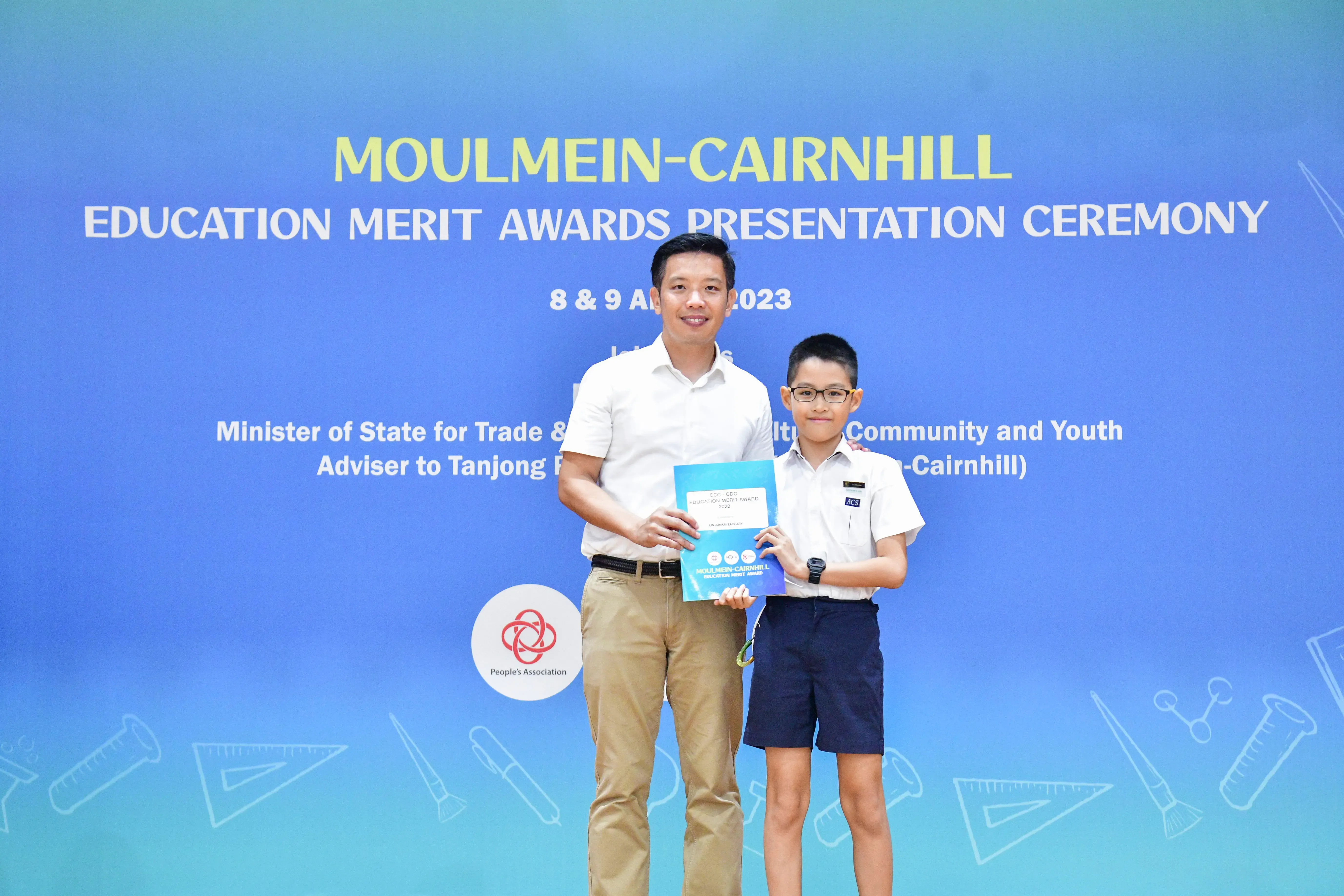 An adult and a young boy in school uniform hold a certificate at the Moulmein-Cairnhill Education Merit Awards 2023.