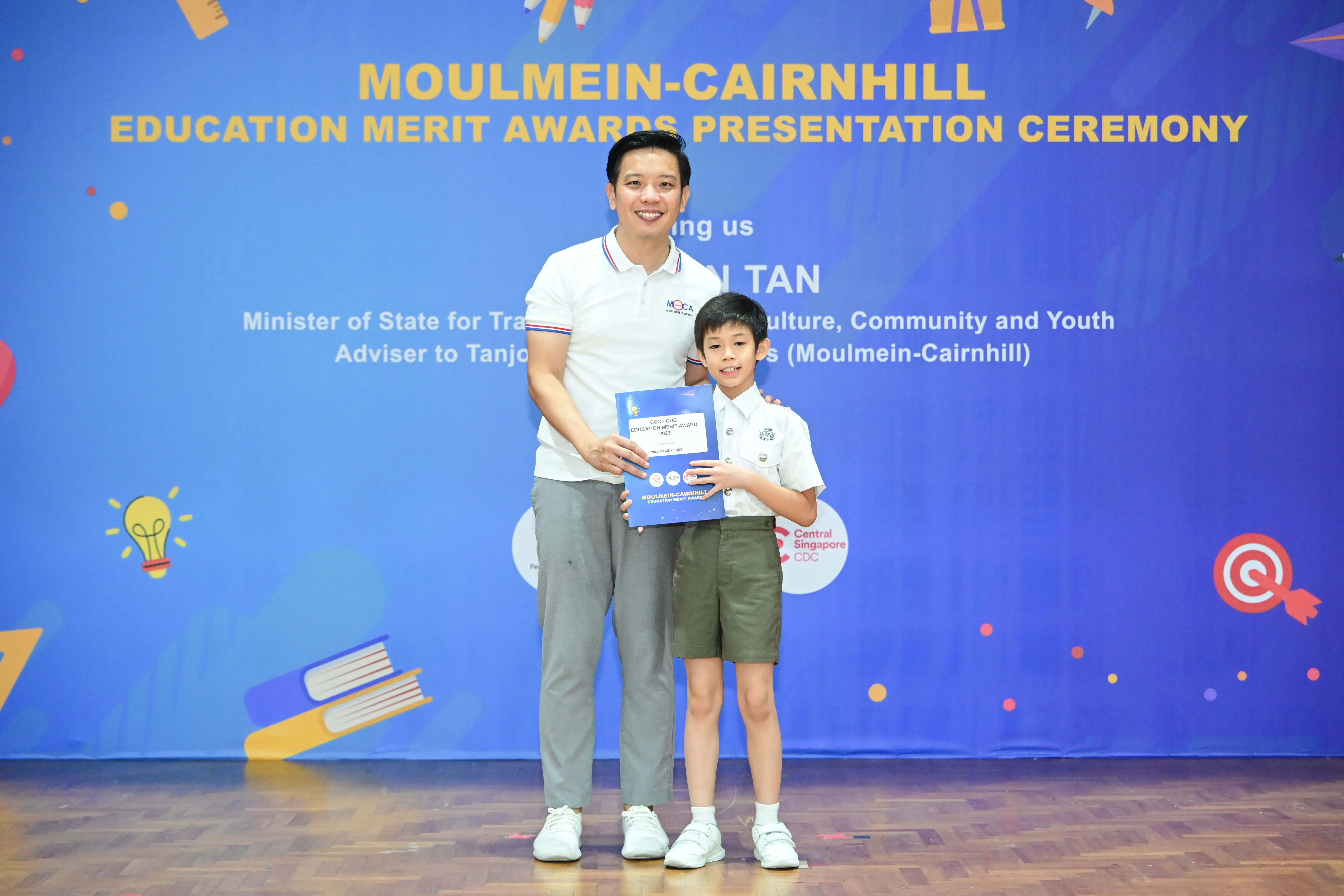 A man and a young boy hold an award certificate at the Moulmein-Cairnhill Education Merit Awards Presentation Ceremony.
