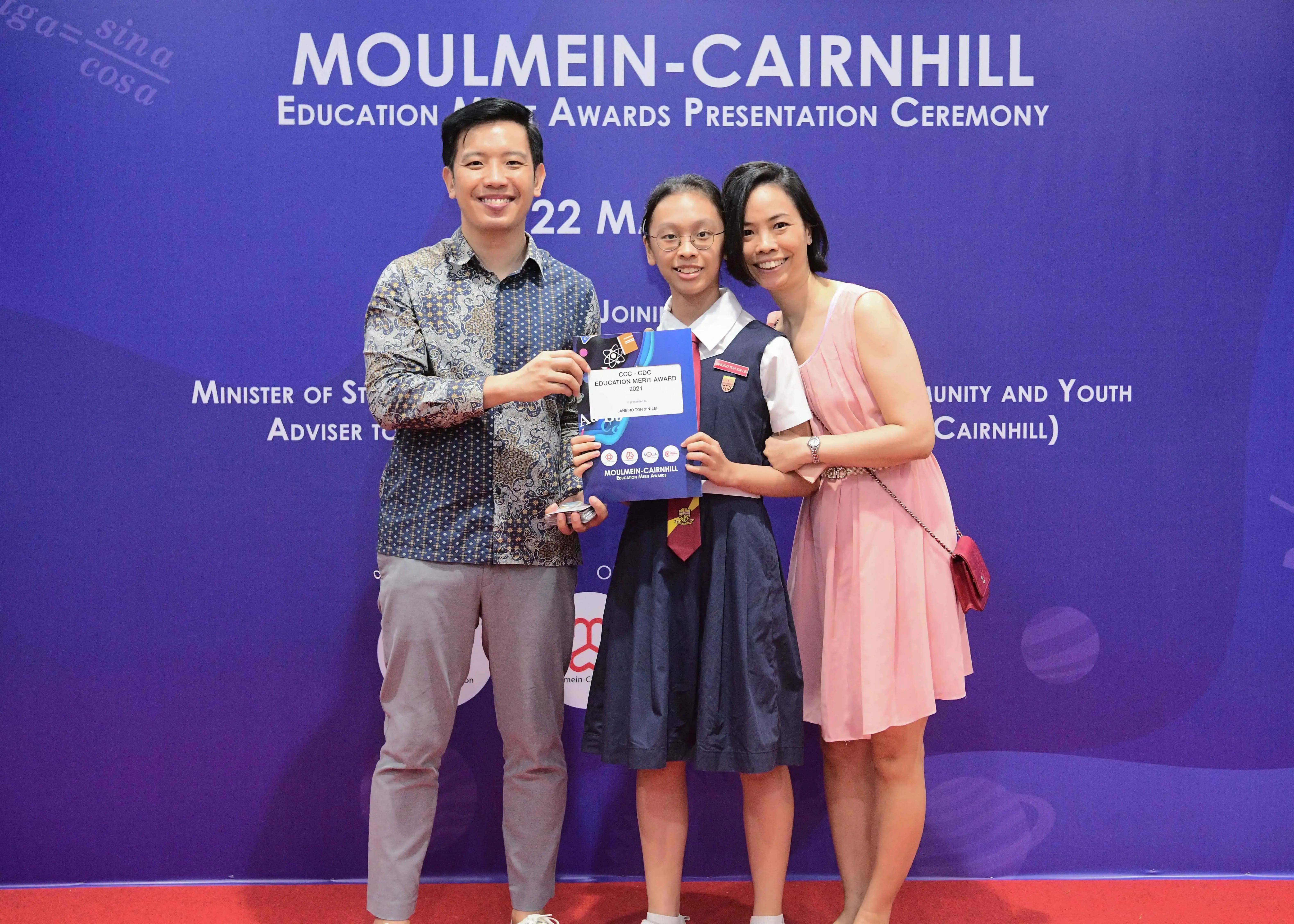 Three smiling people pose with an award certificate at the Moulmein-Cairnhill Education Merit Awards Presentation Ceremony.