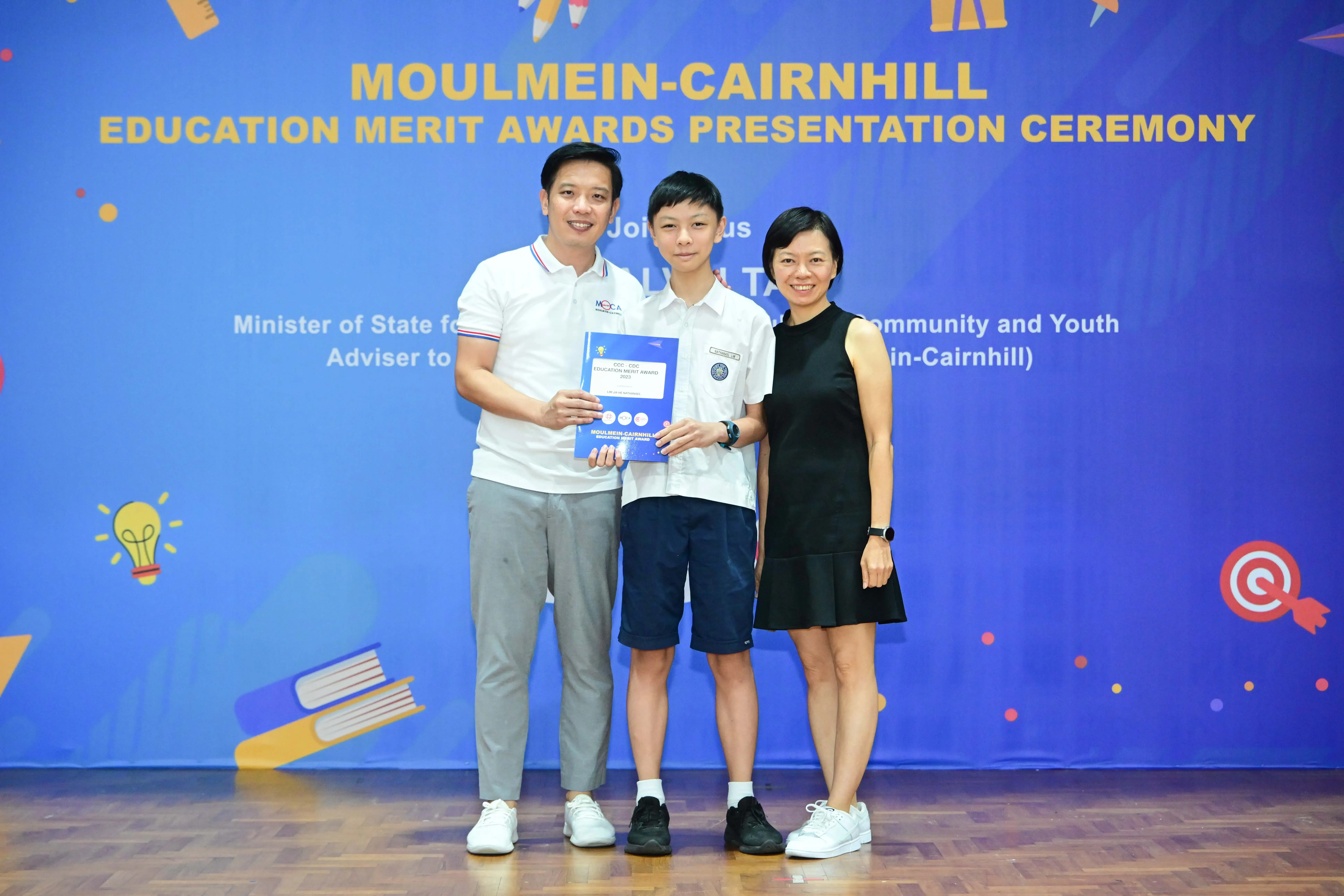 Three people pose holding a certificate at the Moulmein-Cairnhill Education Merit Awards Presentation Ceremony.