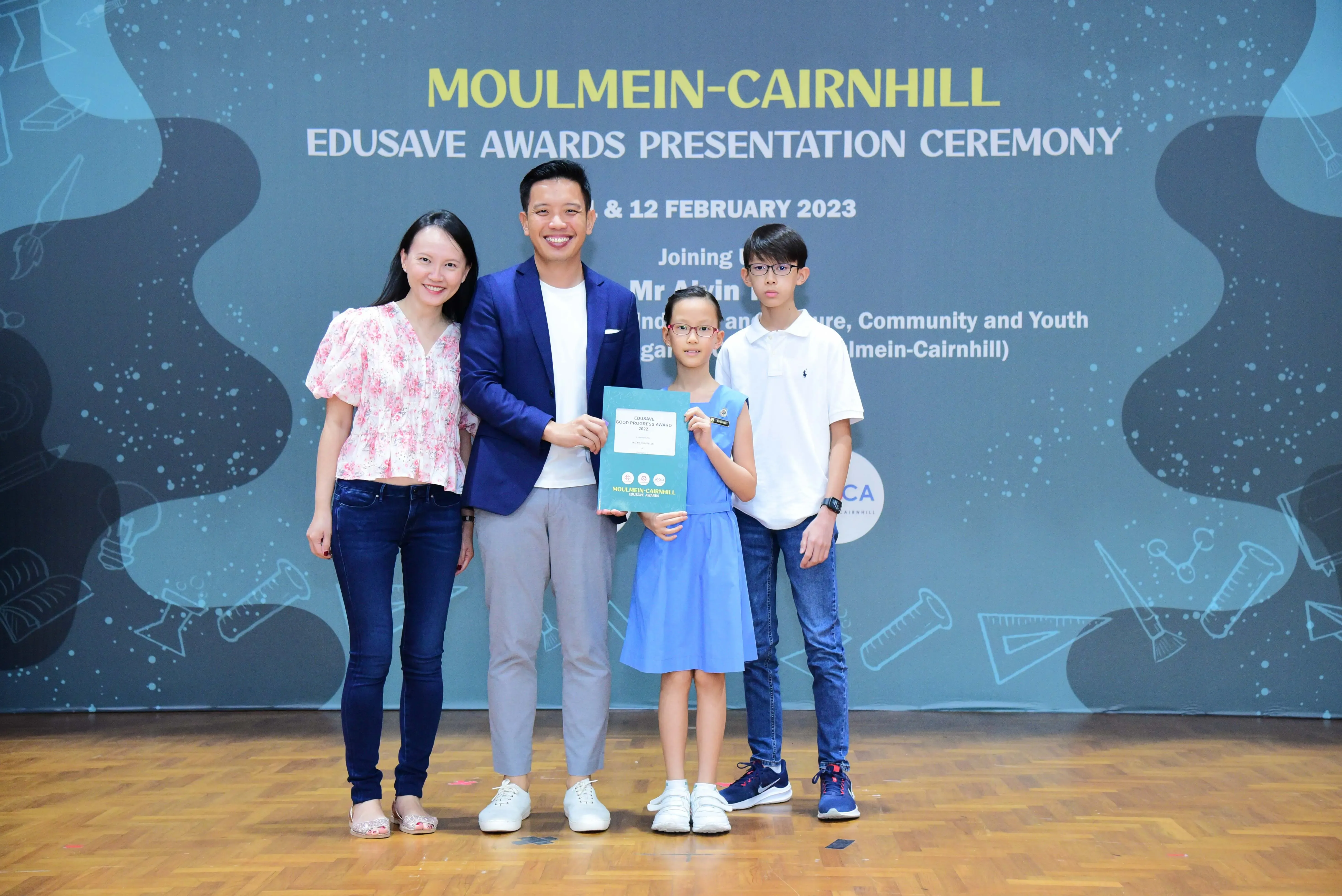 Four people pose on stage at the Moulmein-Cairnhill Edusave Awards Presentation Ceremony, February 2023.