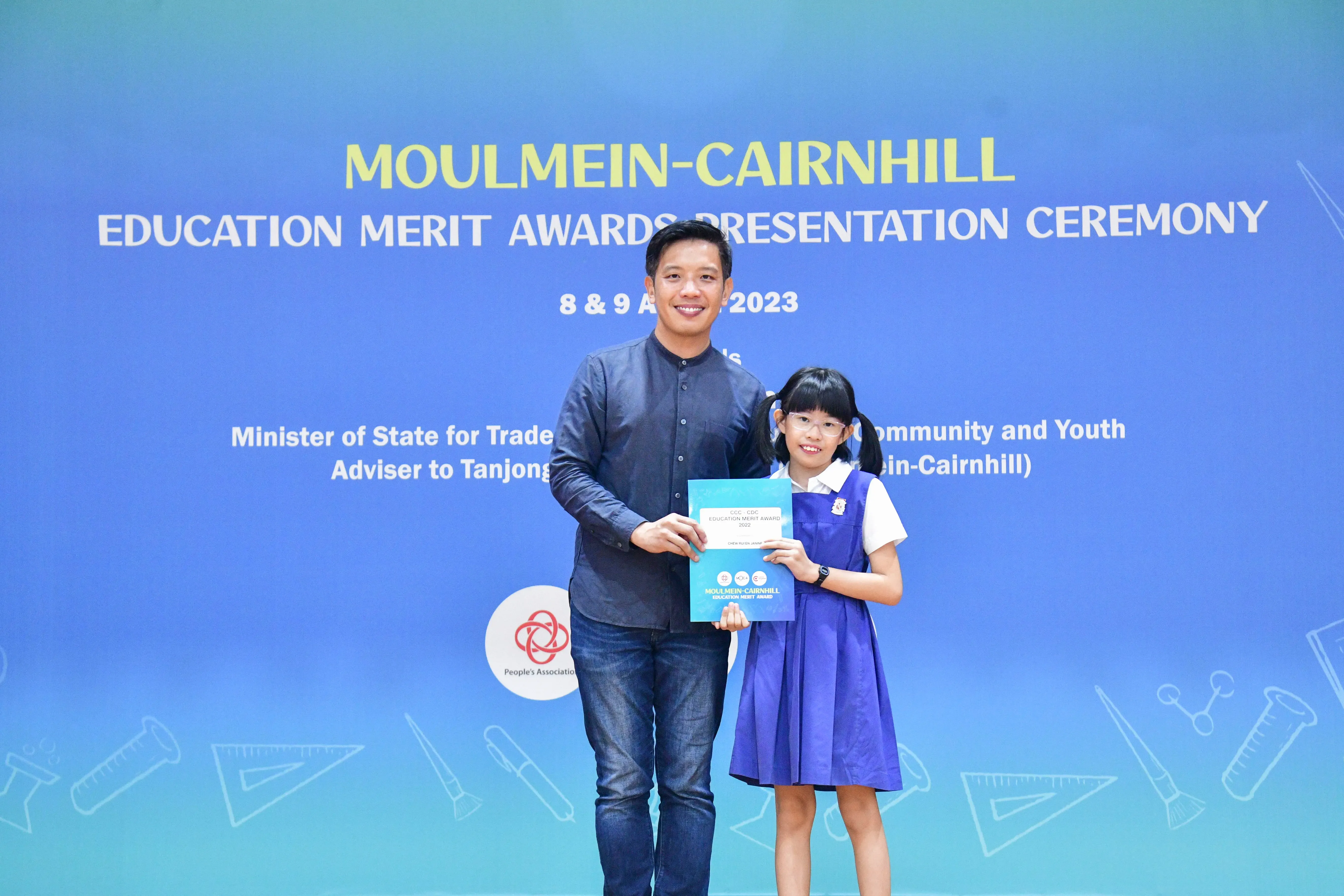 A man and a young girl hold an award certificate at the Moulmein-Cairnhill Education Merit Awards Ceremony 2023.