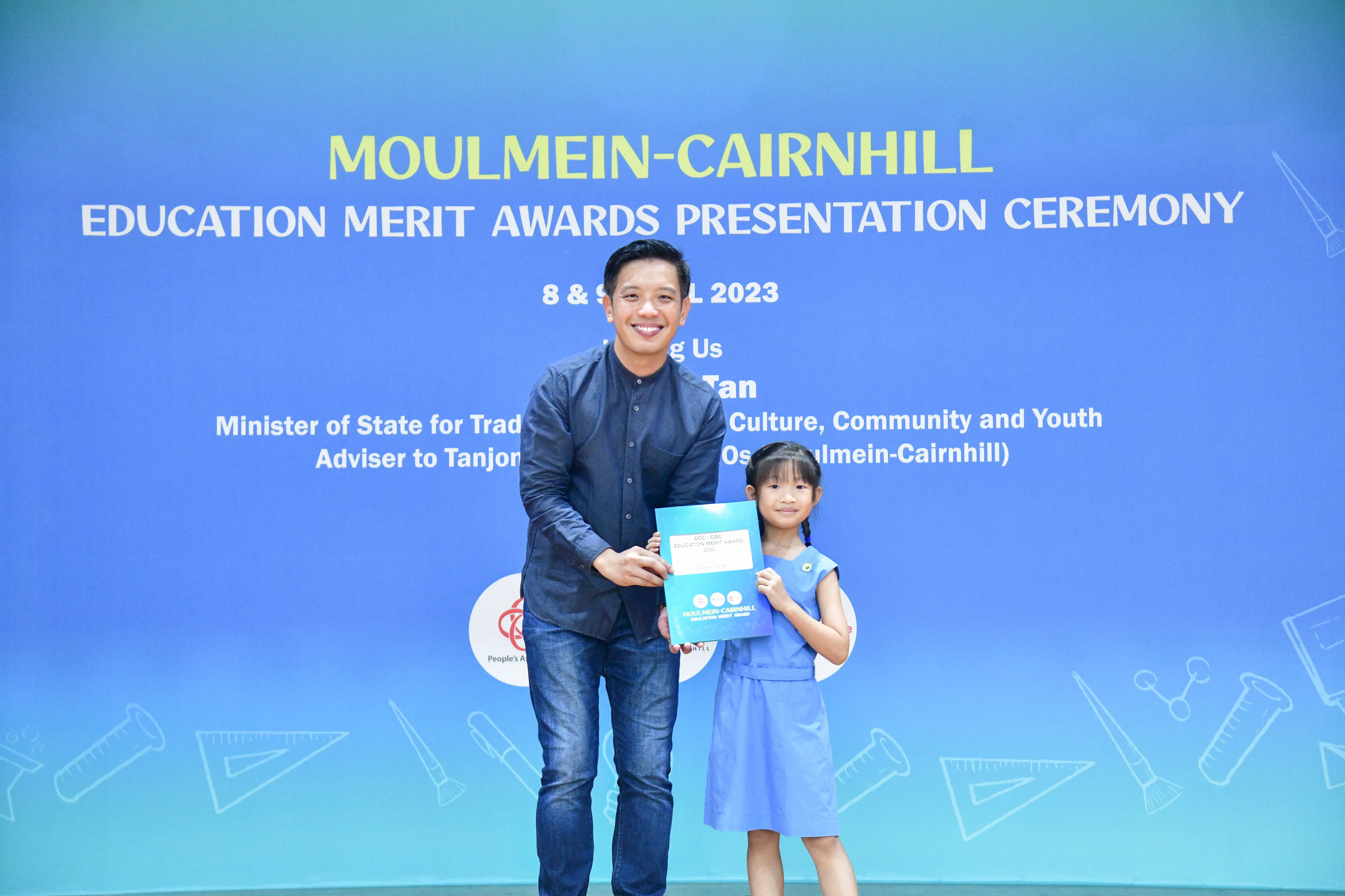 A man and a young girl hold an award certificate at the Moulmein-Cairnhill Education Merit Awards Ceremony 2023.