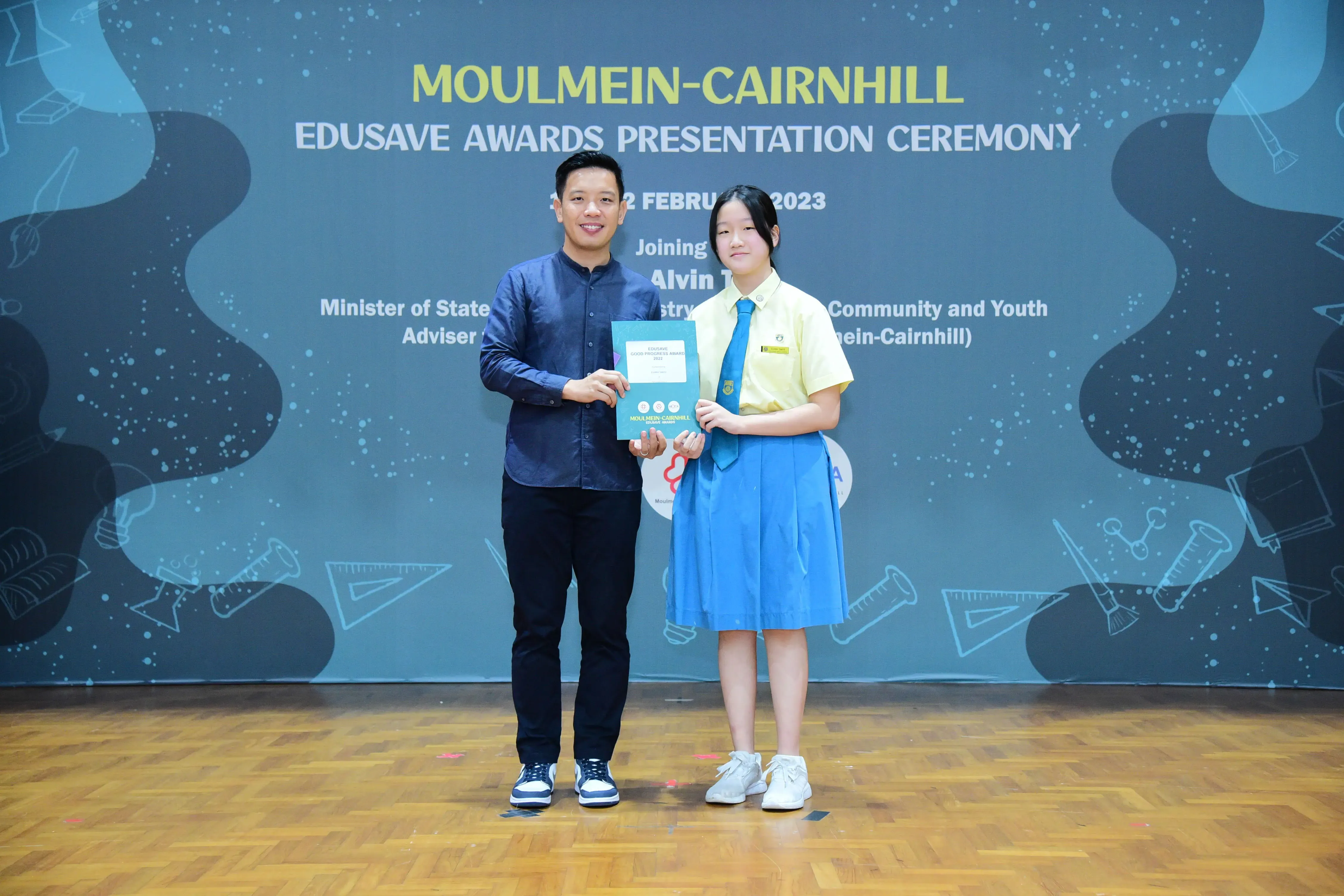 A man and a uniformed schoolgirl hold an award certificate at the Moulmein-Cairnhill Edusave Awards Ceremony 2023.