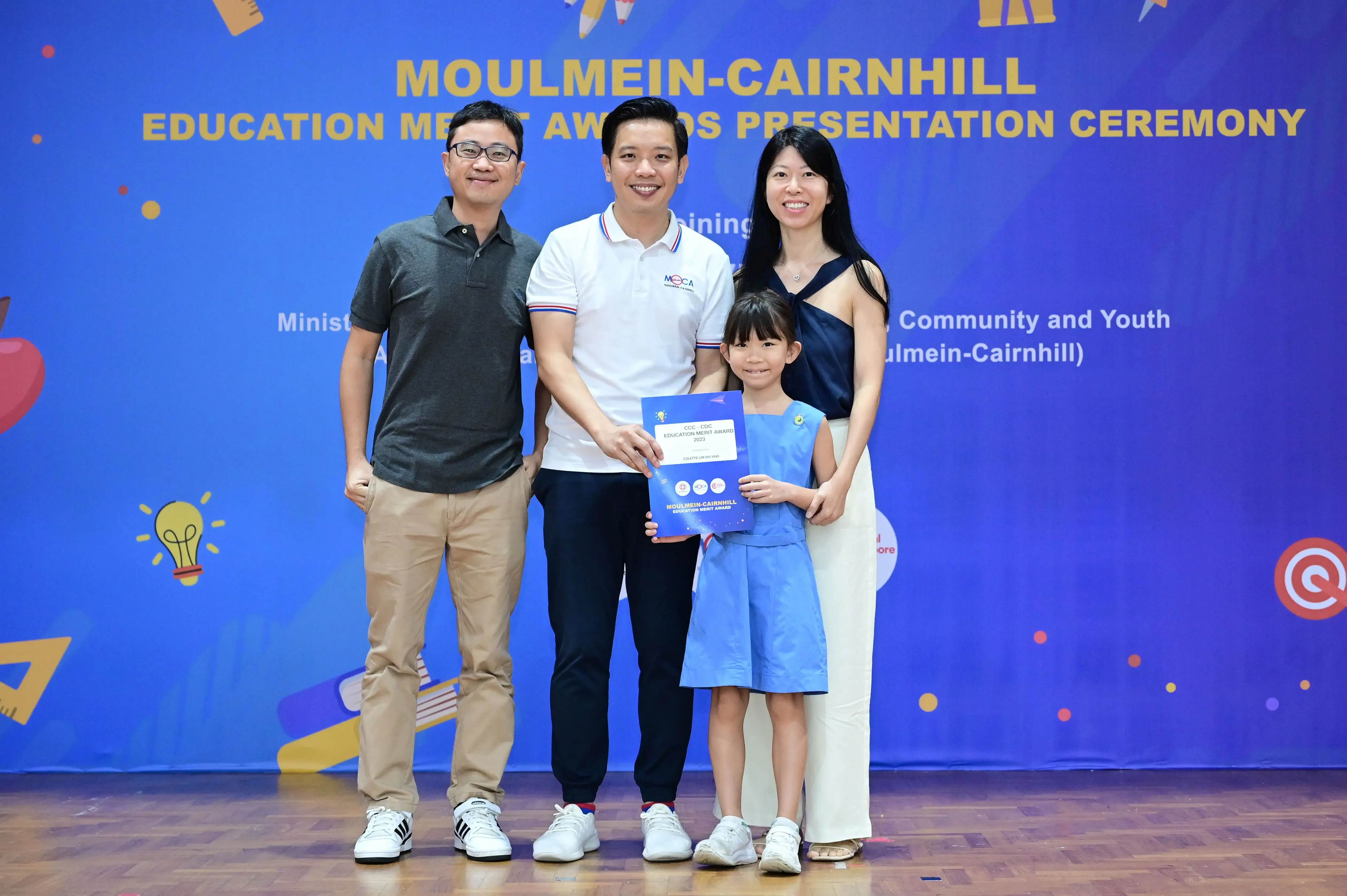 Three adults and a young girl hold a certificate at the Moulmein-Cairnhill Education Merit Awards Presentation Ceremony.