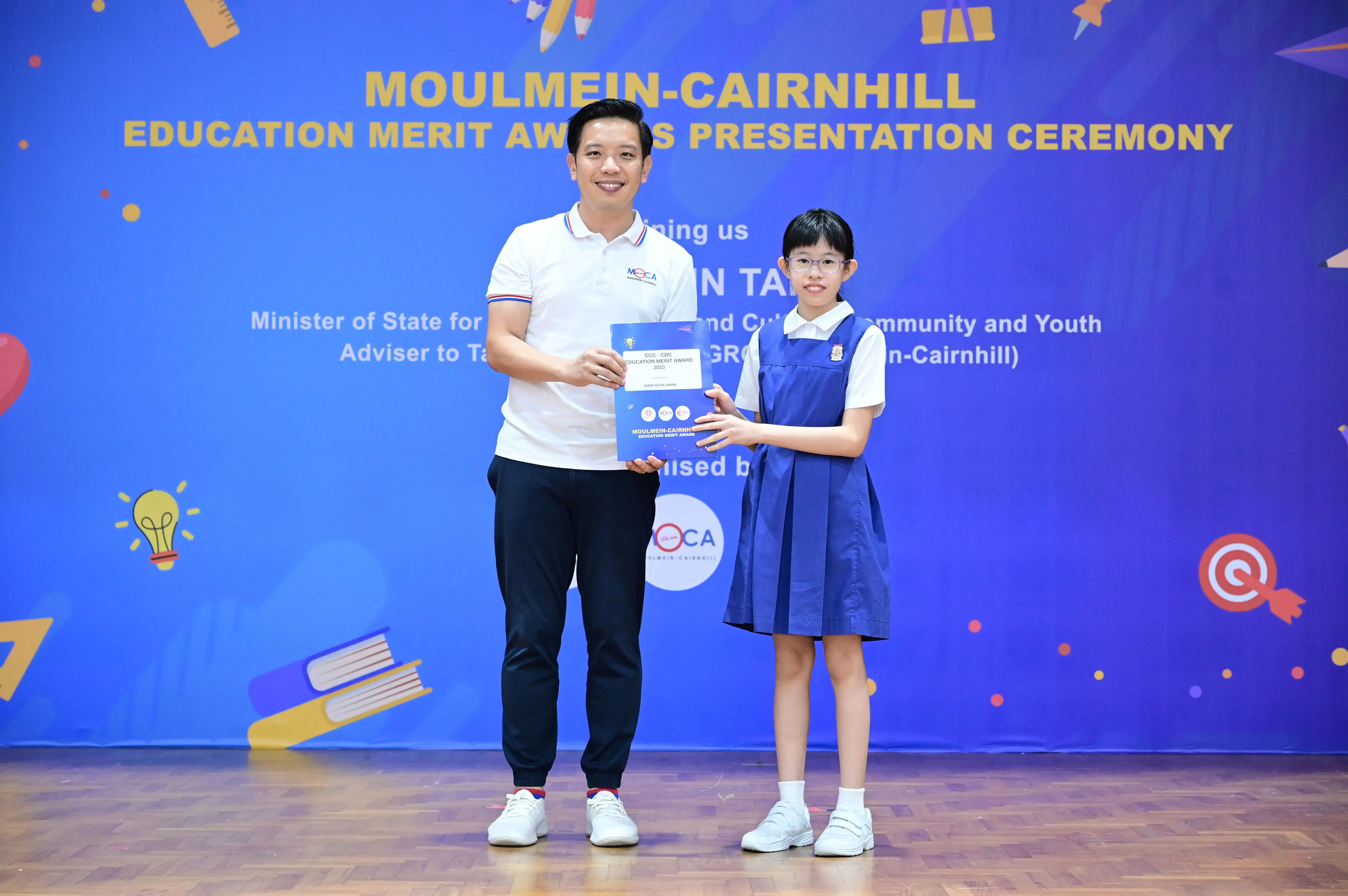 A man and a young girl in school uniform hold a certificate at the Moulmein-Cairnhill Education Merit Awards ceremony.