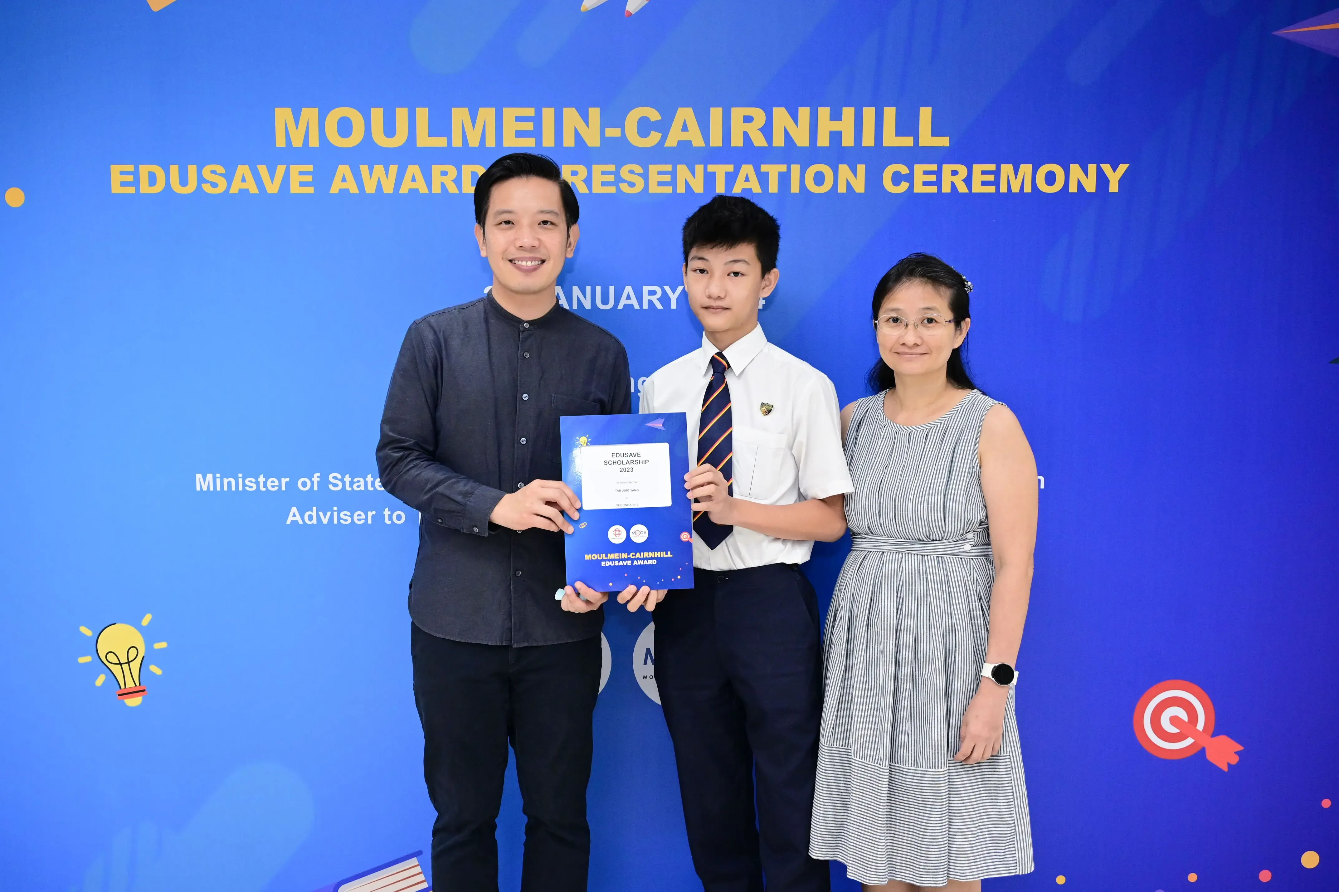Three people pose holding an Edusave Scholarship certificate at the Moulmein-Cairnhill Edusave Award Presentation Ceremony.