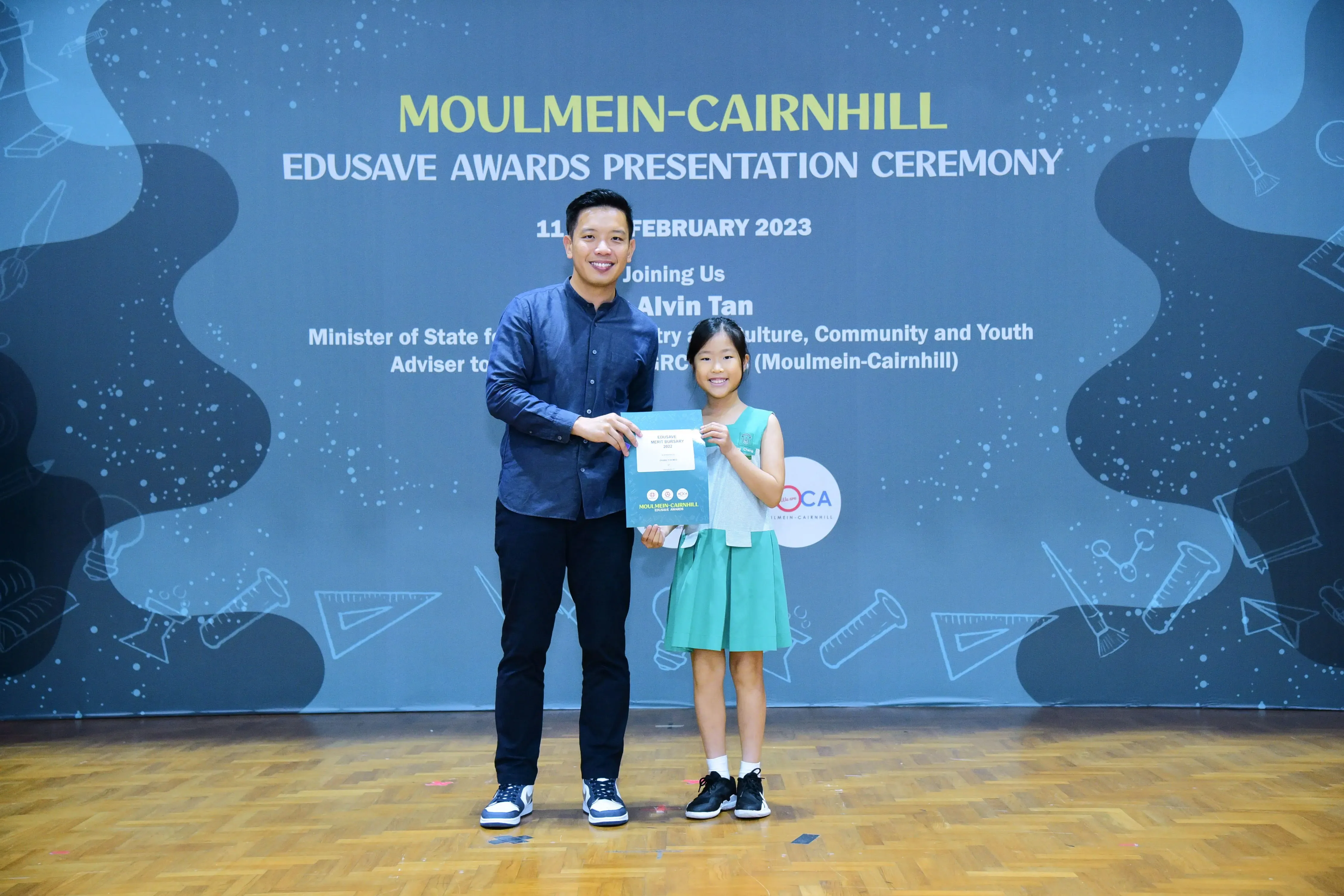A man and a young girl hold a certificate at the Moulmein-Cairnhill Edusave Awards Presentation Ceremony in 2023.