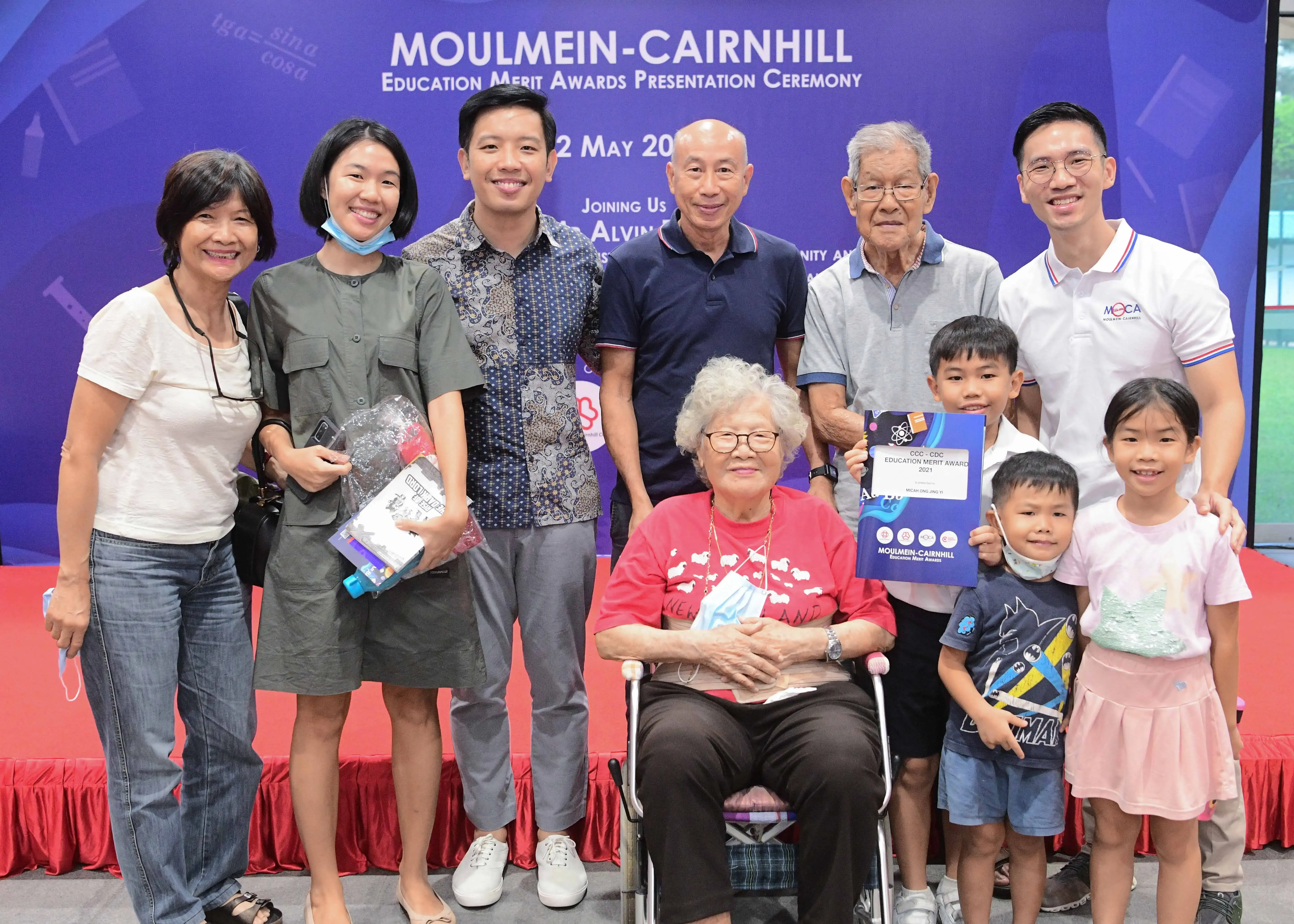 A multigenerational family poses at the Moulmein-Cairnhill Education Merit Awards Presentation Ceremony, holding award certificates.