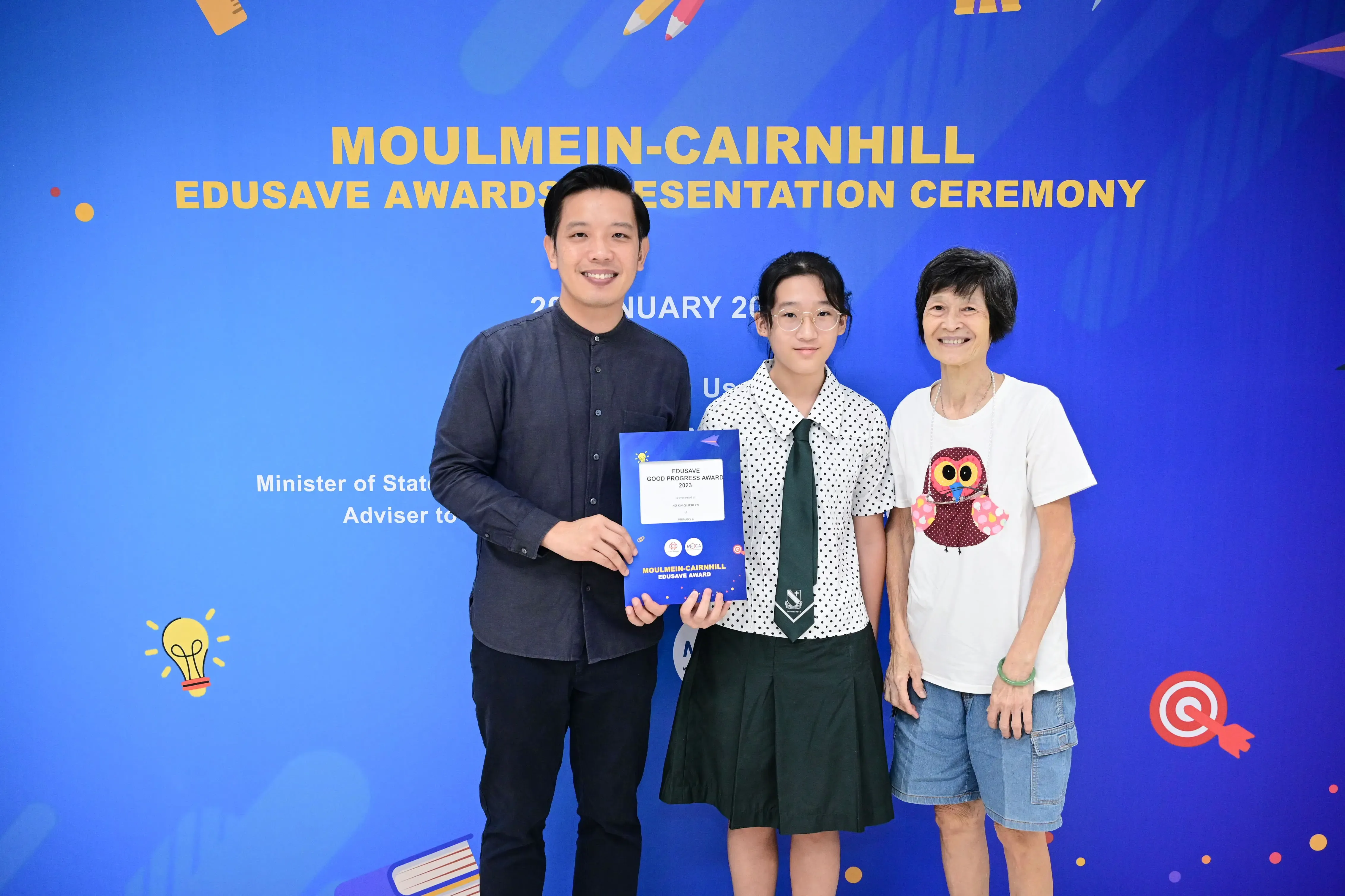 Three people pose together holding an Edusave award certificate at the Moulmein-Cairnhill Edusave Awards Presentation Ceremony.