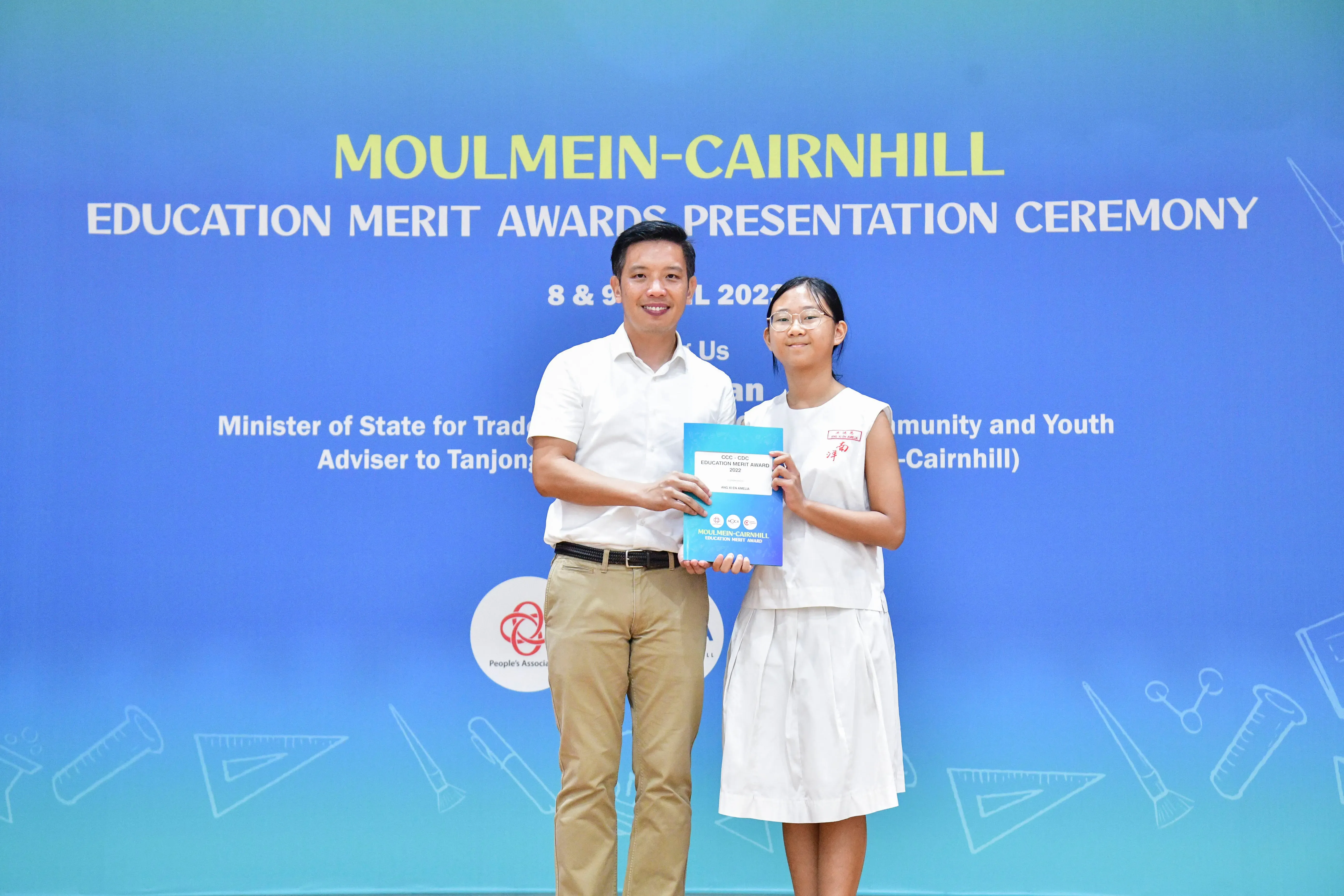 A man and a young girl hold a blue award booklet at the Moulmein-Cairnhill Education Merit Awards Ceremony.
