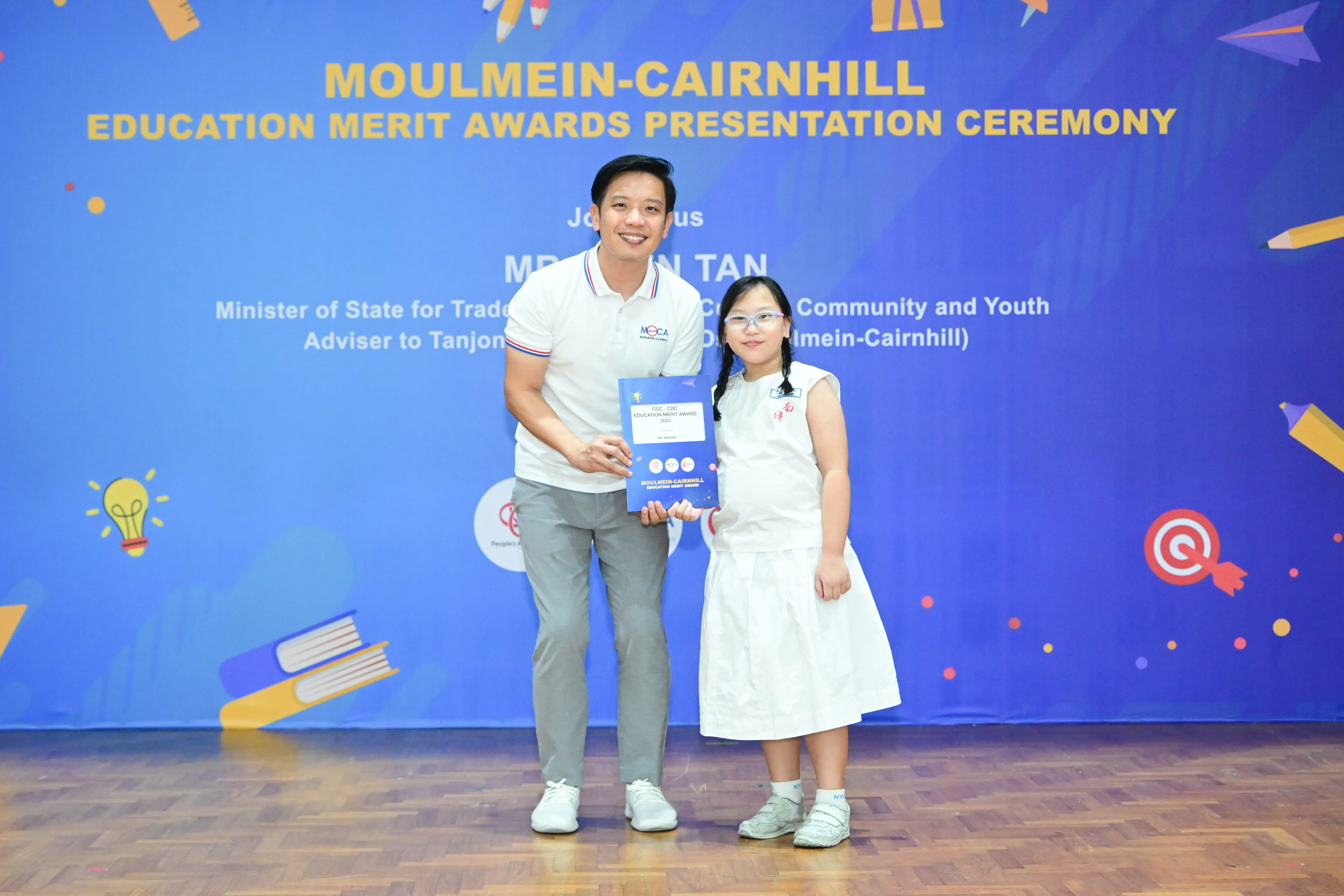 A man and a young girl hold an award certificate at the Moulmein-Cairnhill Education Merit Awards Presentation Ceremony.