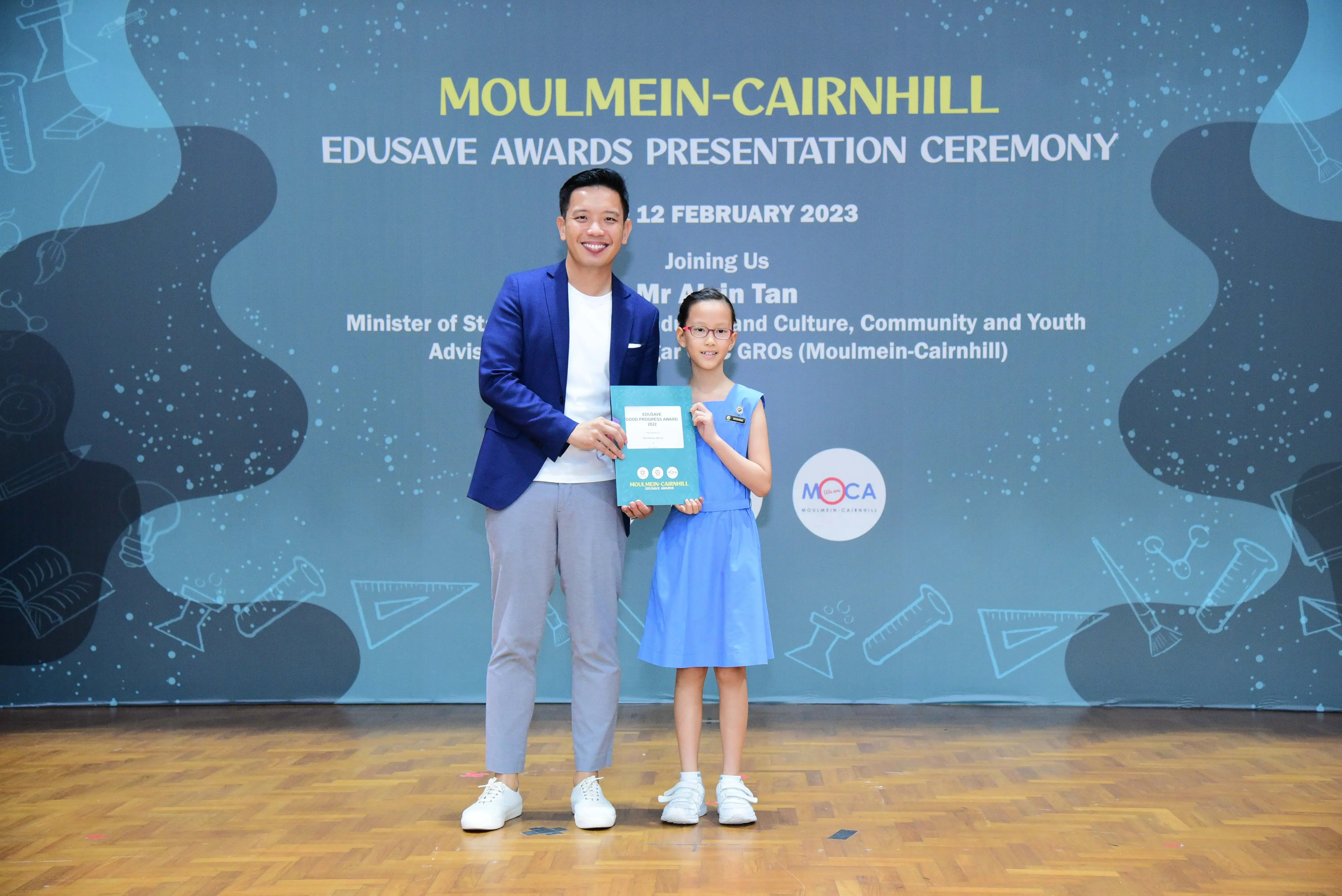 A man in a blue blazer and a young girl hold a certificate at the Moulmein-Cairnhill Edusave Awards Ceremony 2023.