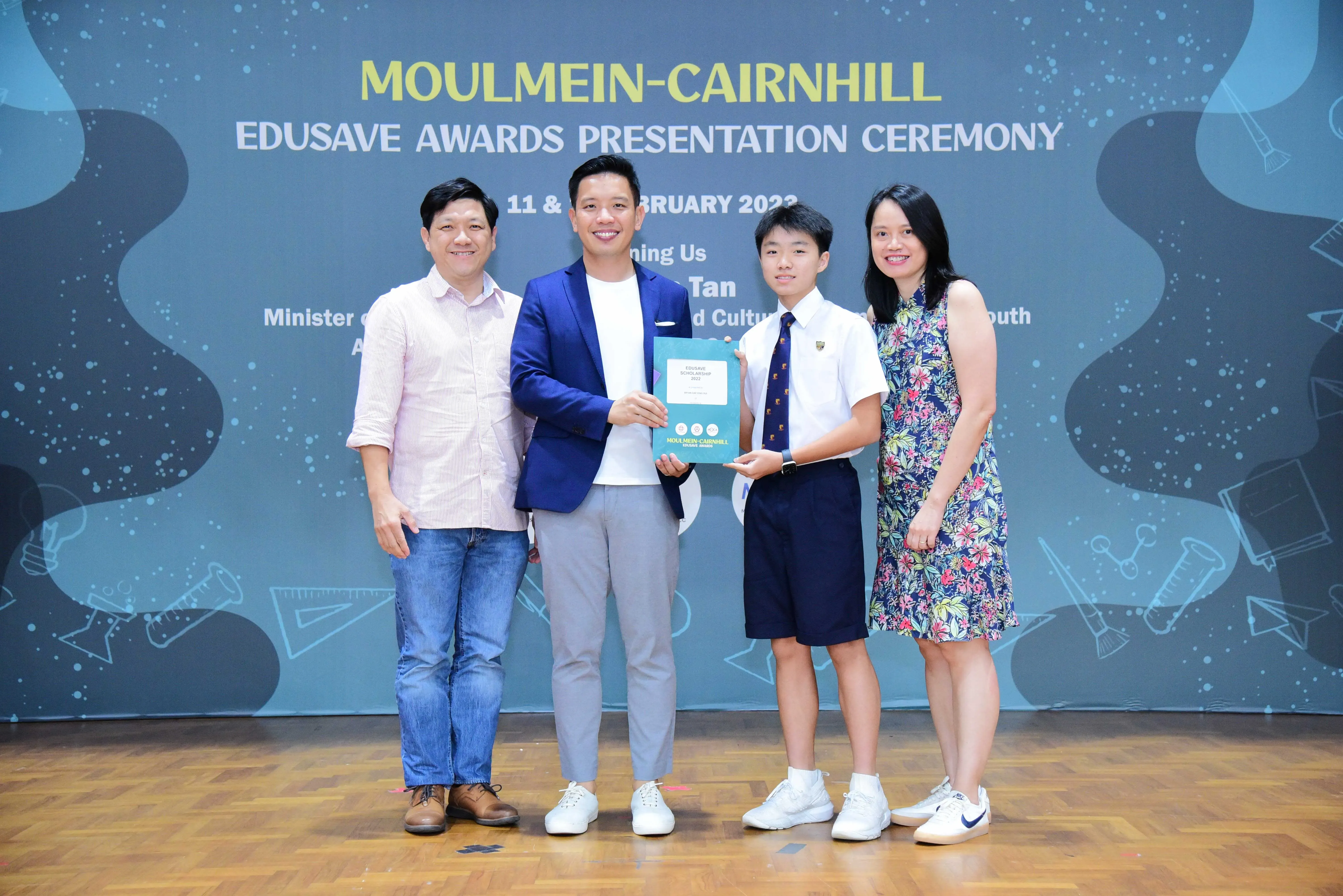 Four people pose together at the Moulmein-Cairnhill Edusave Awards Presentation Ceremony, with a student holding an award.
