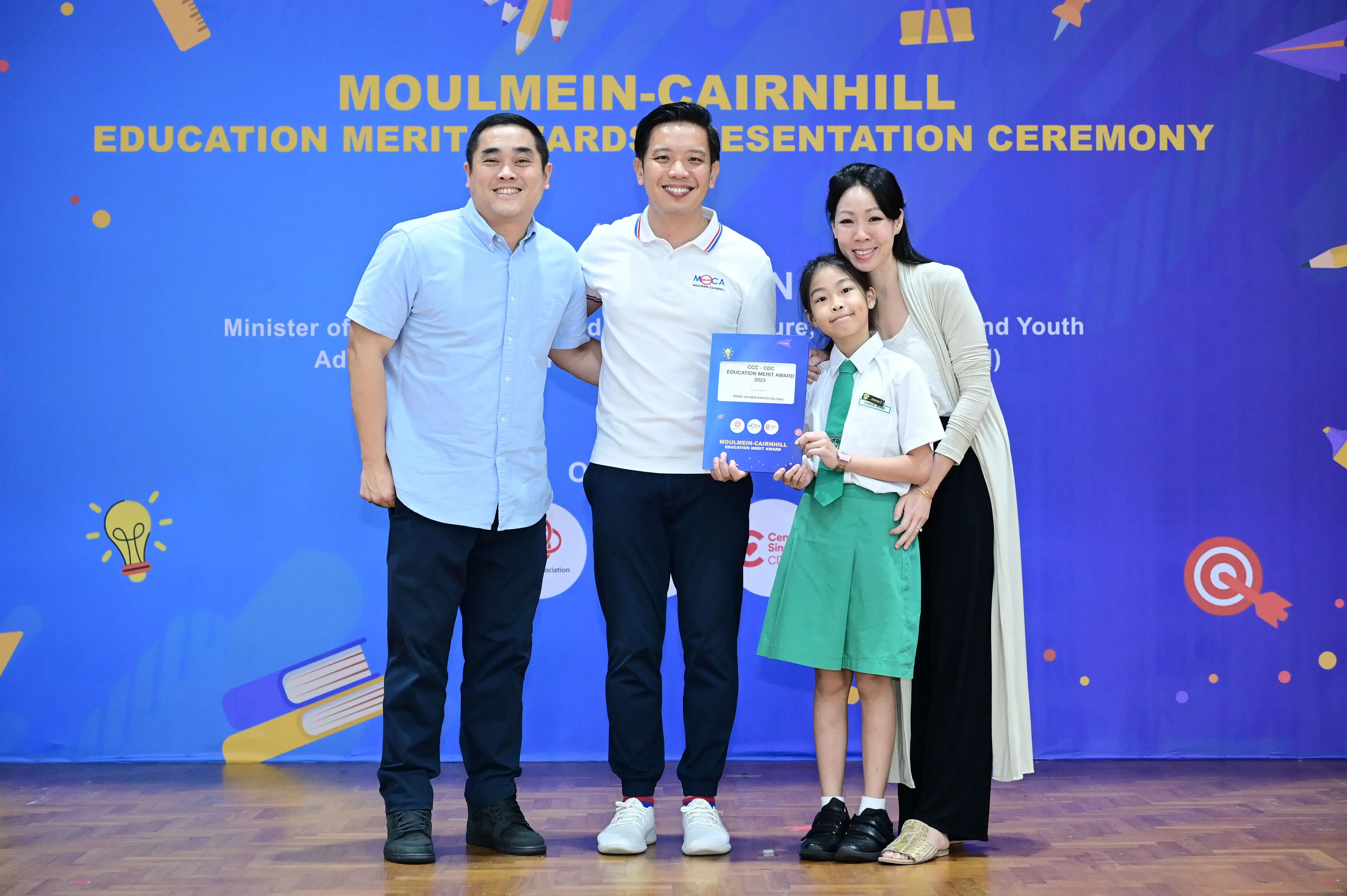Three adults and a young girl in school uniform pose at the Moulmein-Cairnhill Education Merit Awards ceremony.