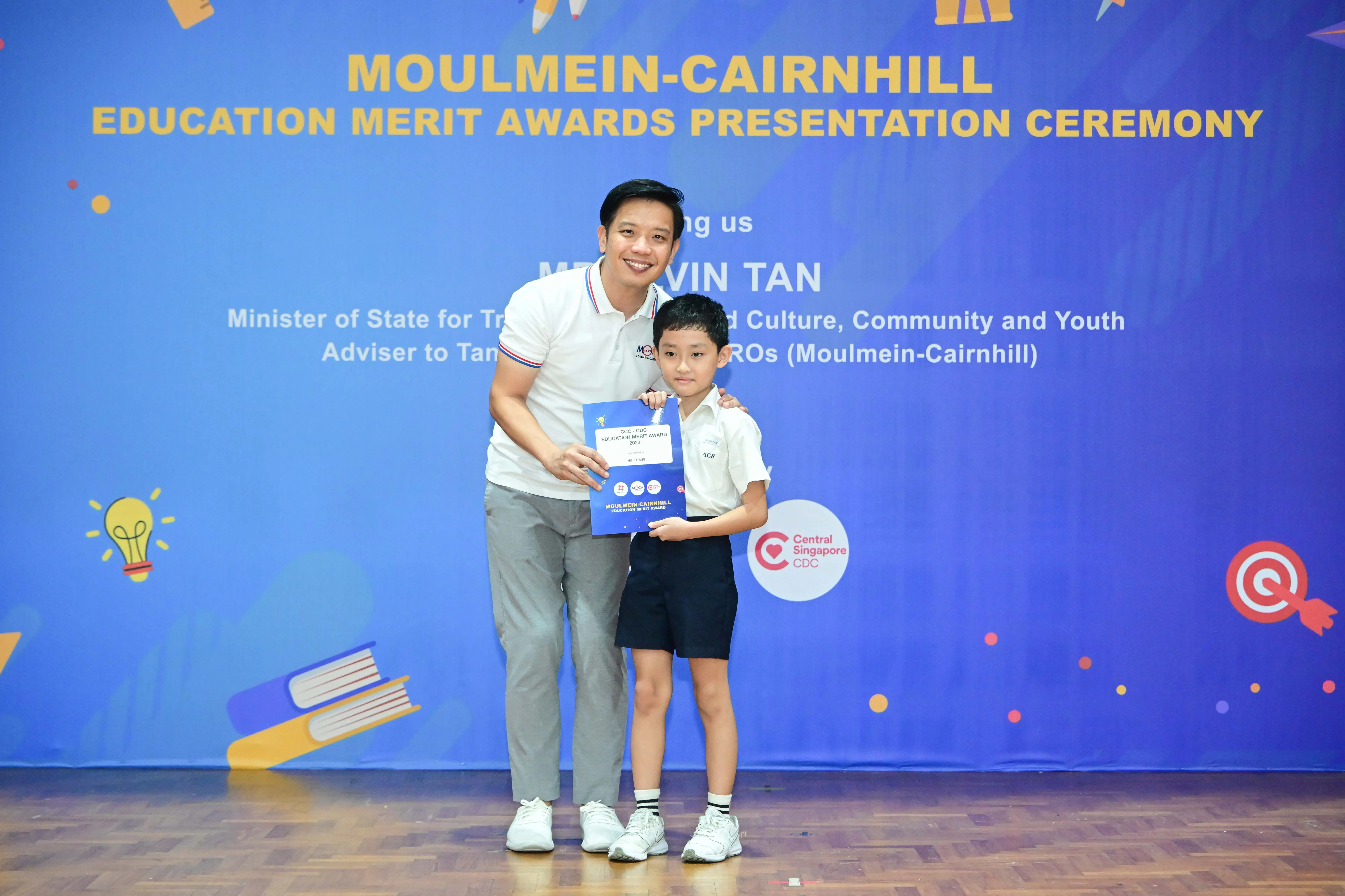 A man and a young boy hold an award certificate at the Moulmein-Cairnhill Education Merit Awards Ceremony.