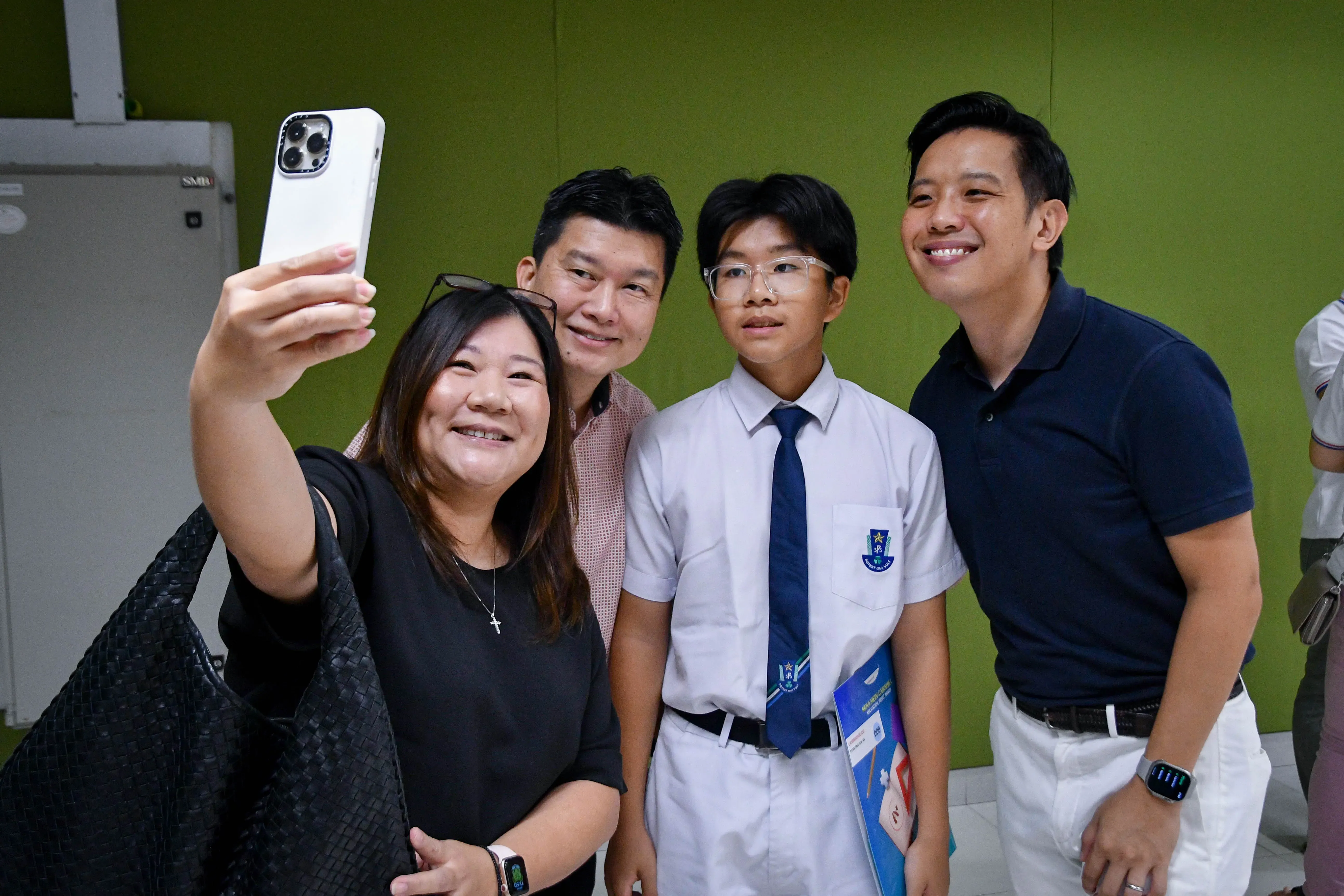 Four people pose for a selfie, including a young student in a white uniform with a blue tie.