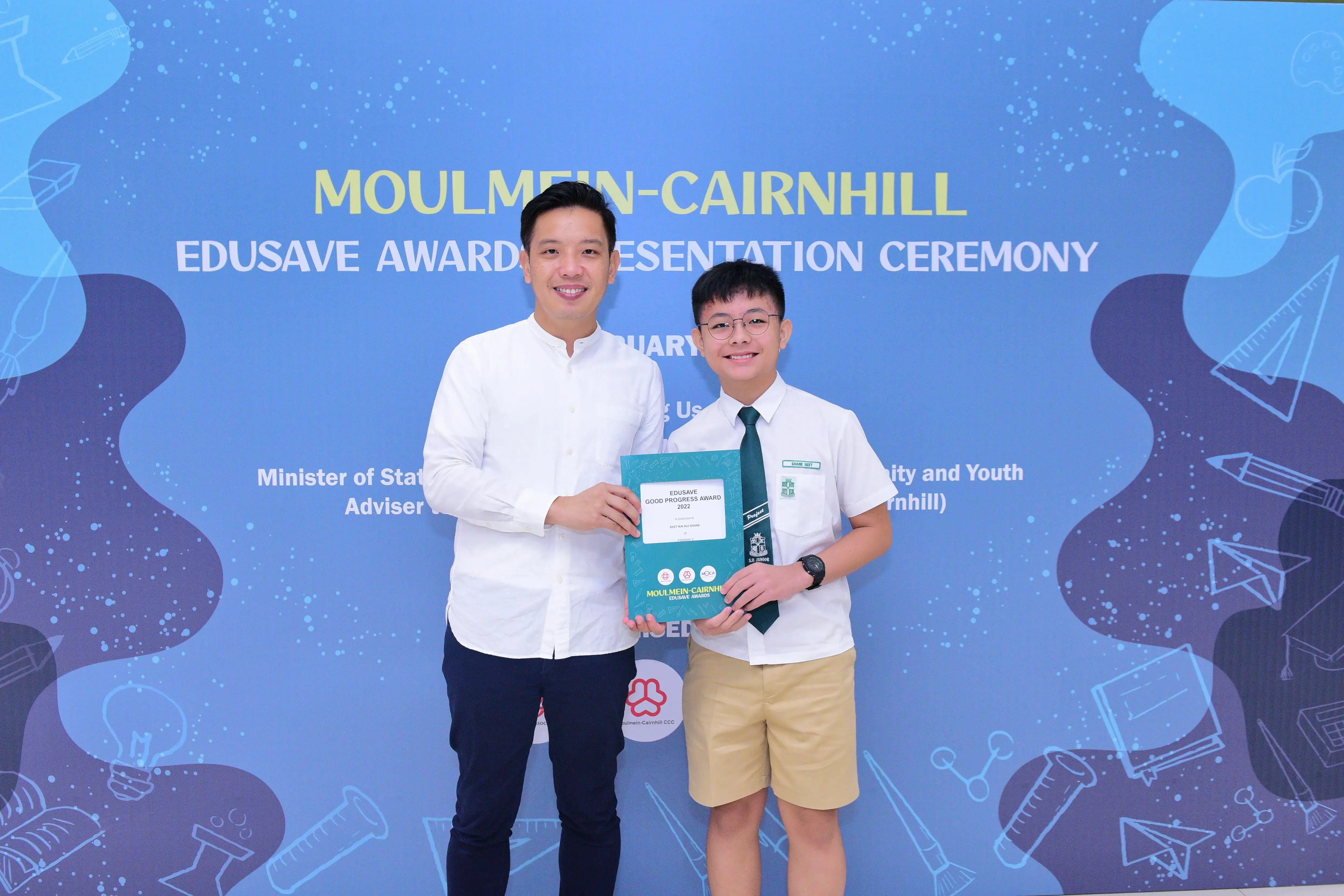 An adult and a young student in uniform hold an Edusave Good Progress Award at the Moulmein-Cairnhill ceremony.