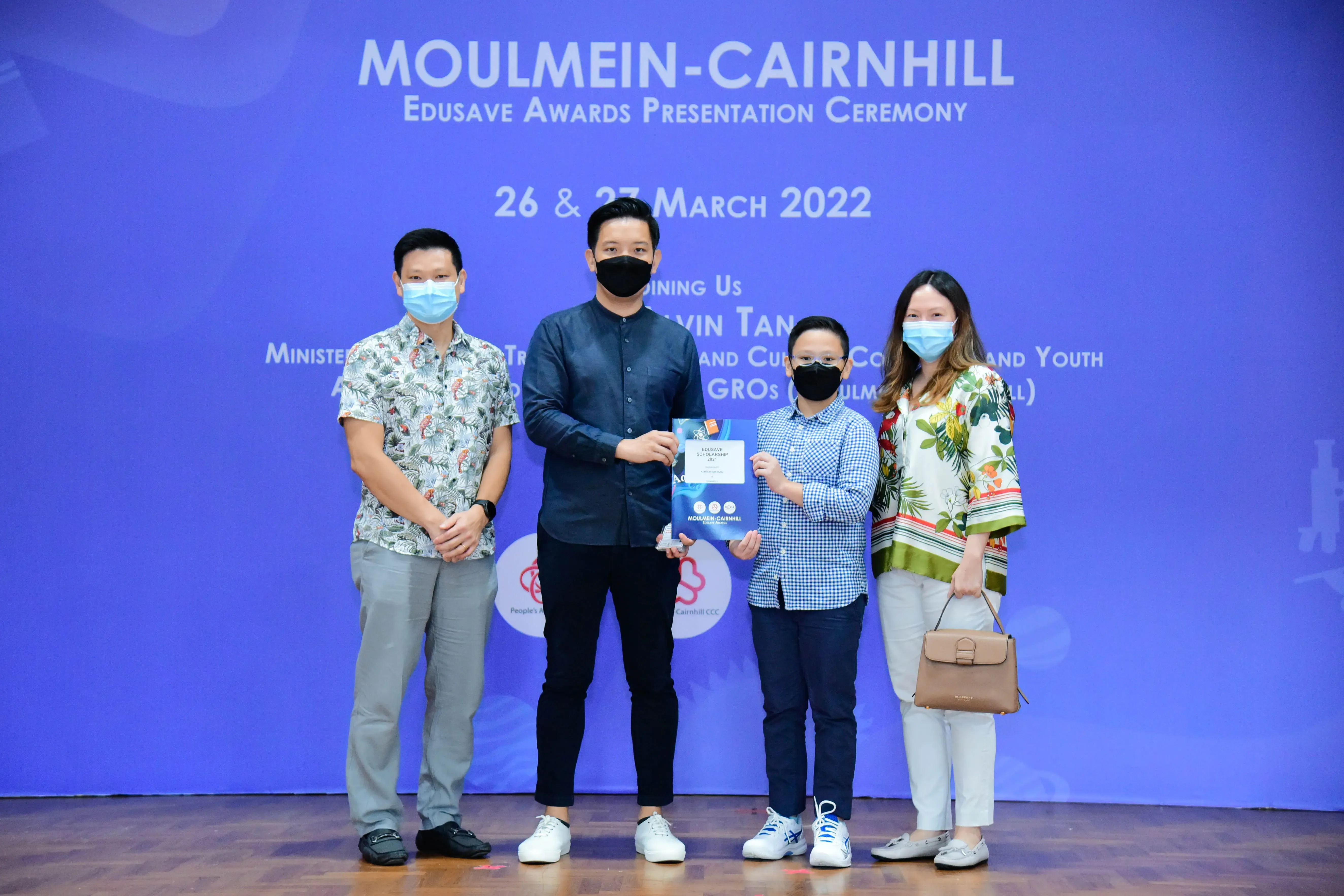 Four masked people stand on stage at the Moulmein-Cairnhill Edusave Awards Presentation Ceremony, March 2022.