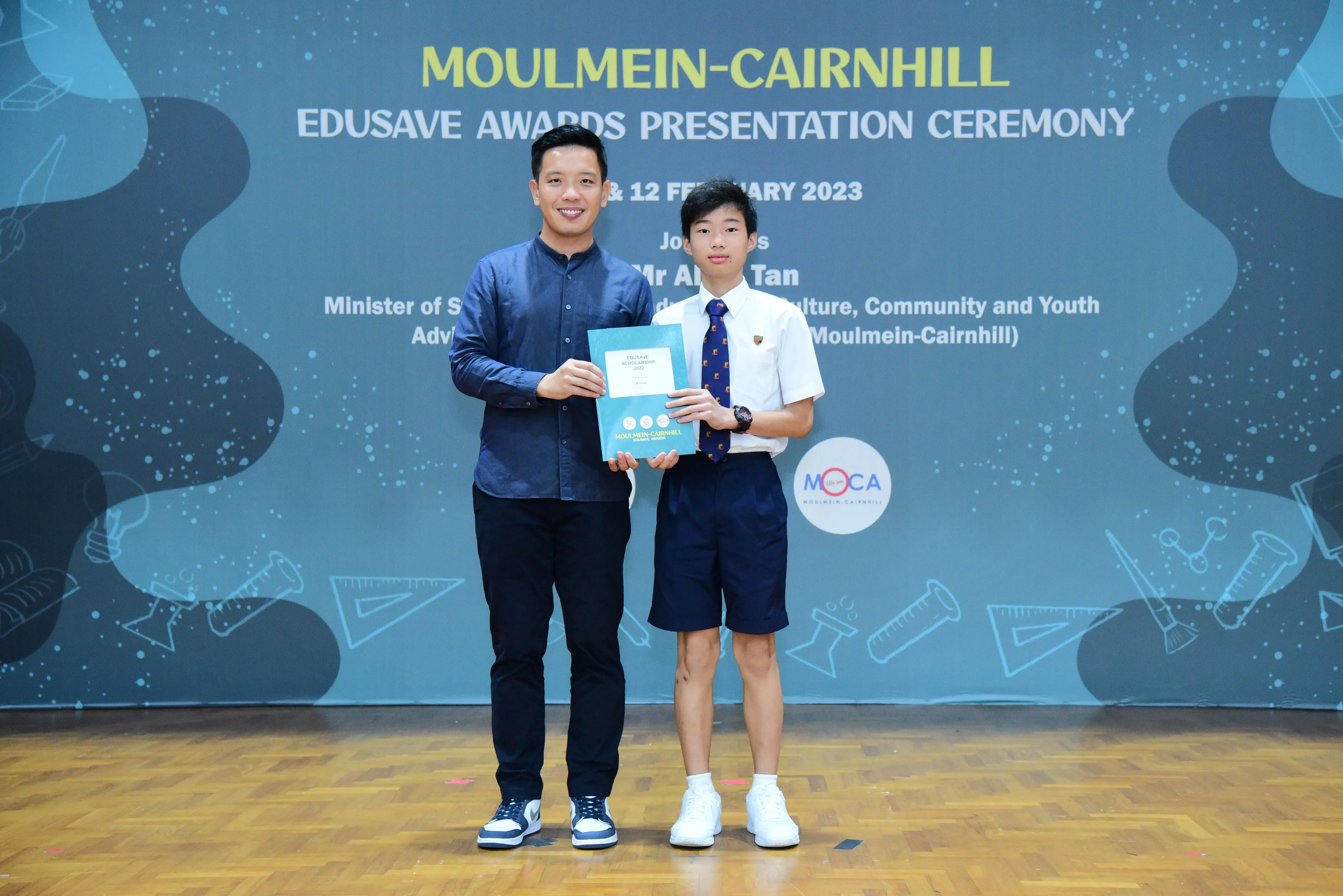 Two people hold an award certificate at the Moulmein-Cairnhill Edusave Awards Presentation Ceremony 2023.