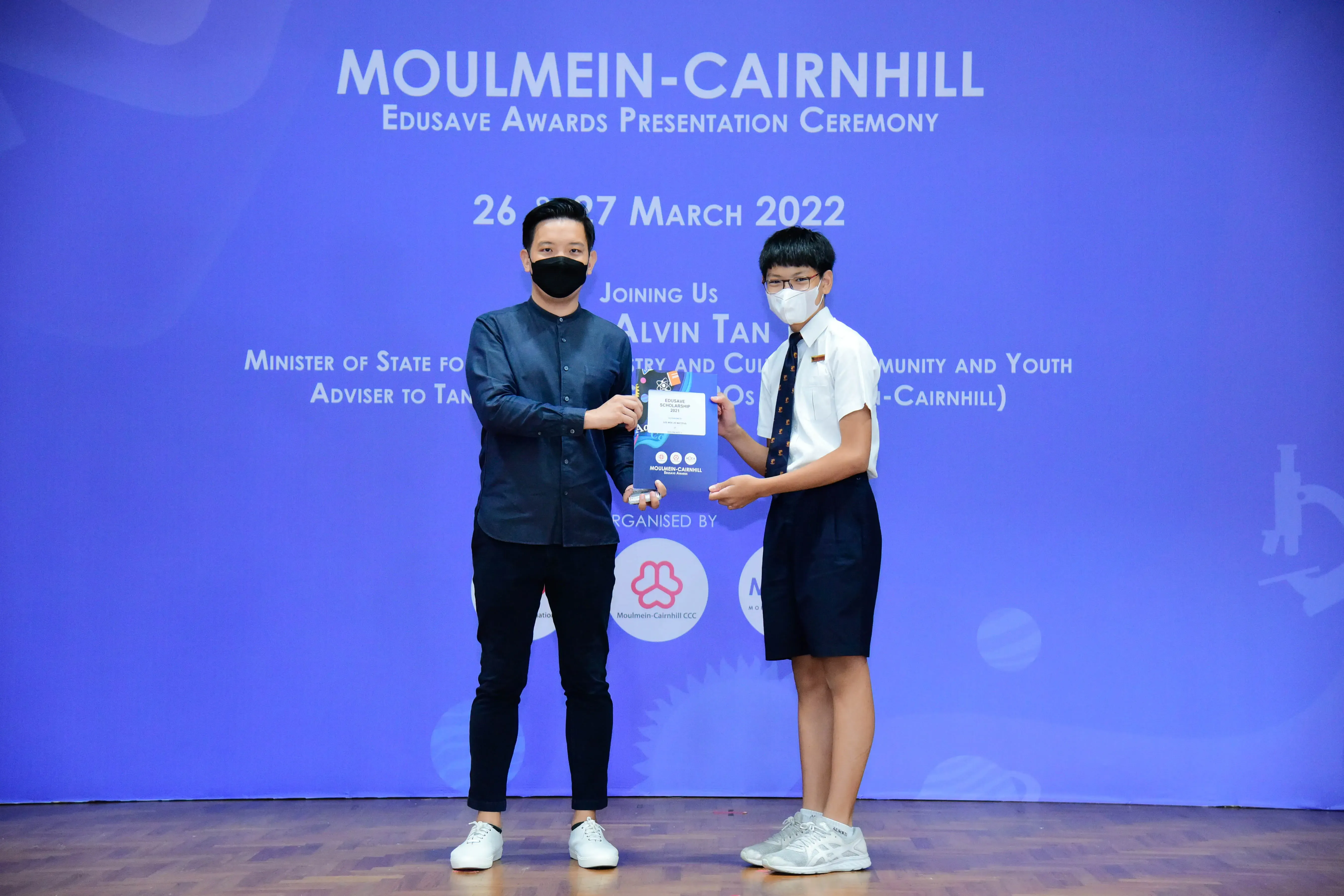 Two masked people hold a certificate at the Moulmein-Cairnhill Edusave Awards Presentation Ceremony, March 2022.