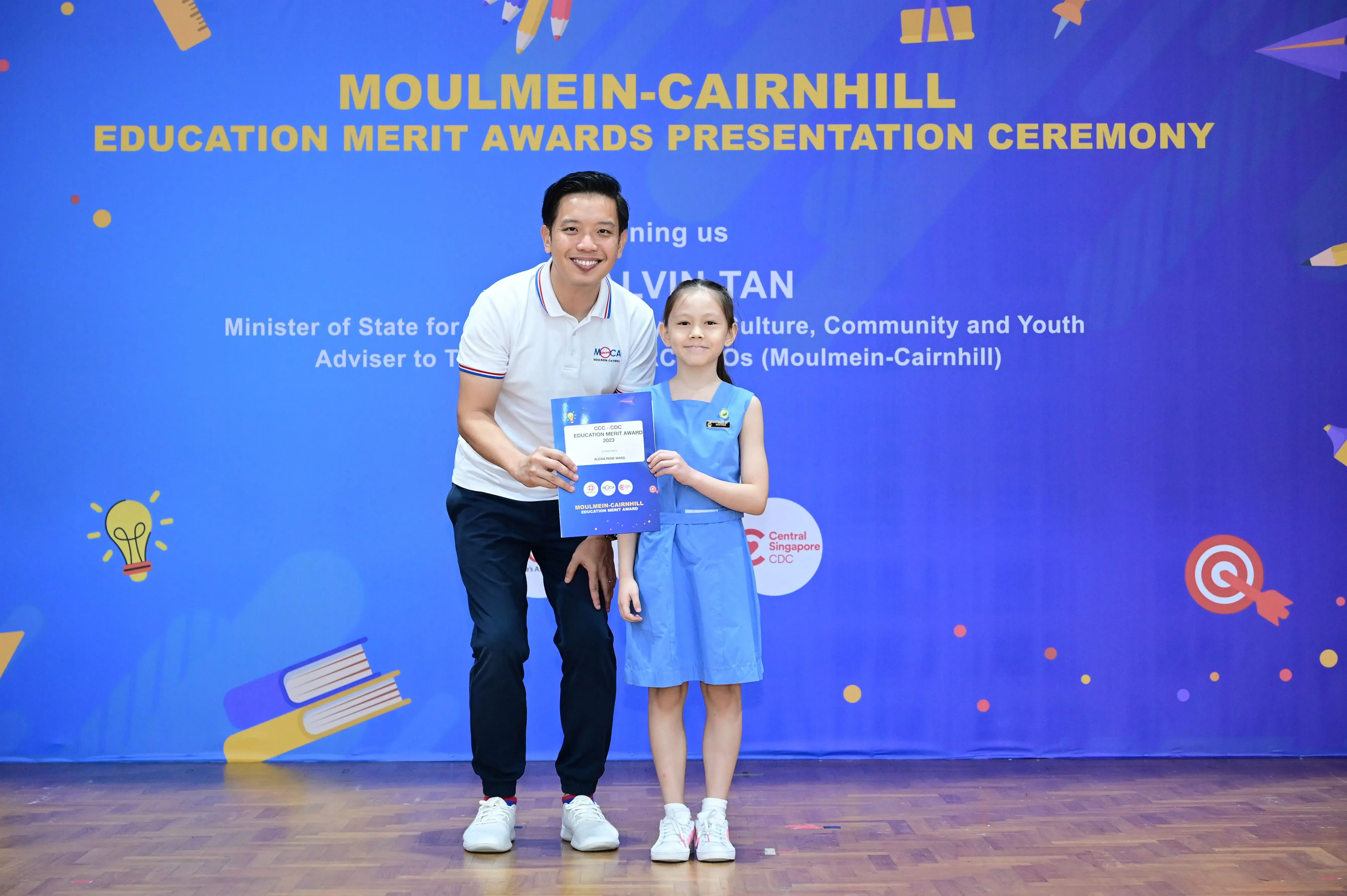 A man and a young girl hold a certificate at the Moulmein-Cairnhill Education Merit Awards ceremony.