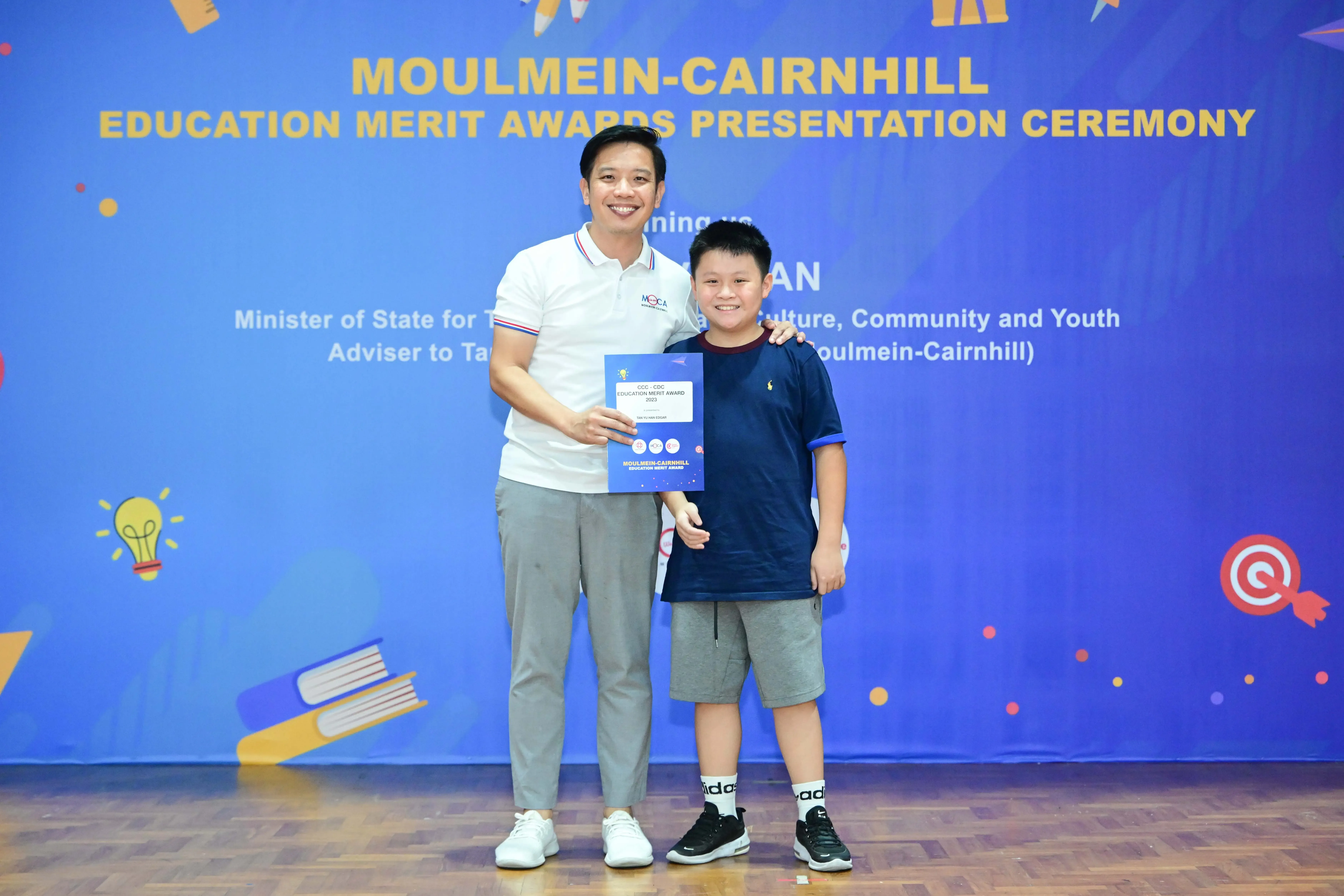 A man and a young boy pose holding an award certificate at the Moulmein-Cairnhill Education Merit Awards ceremony.