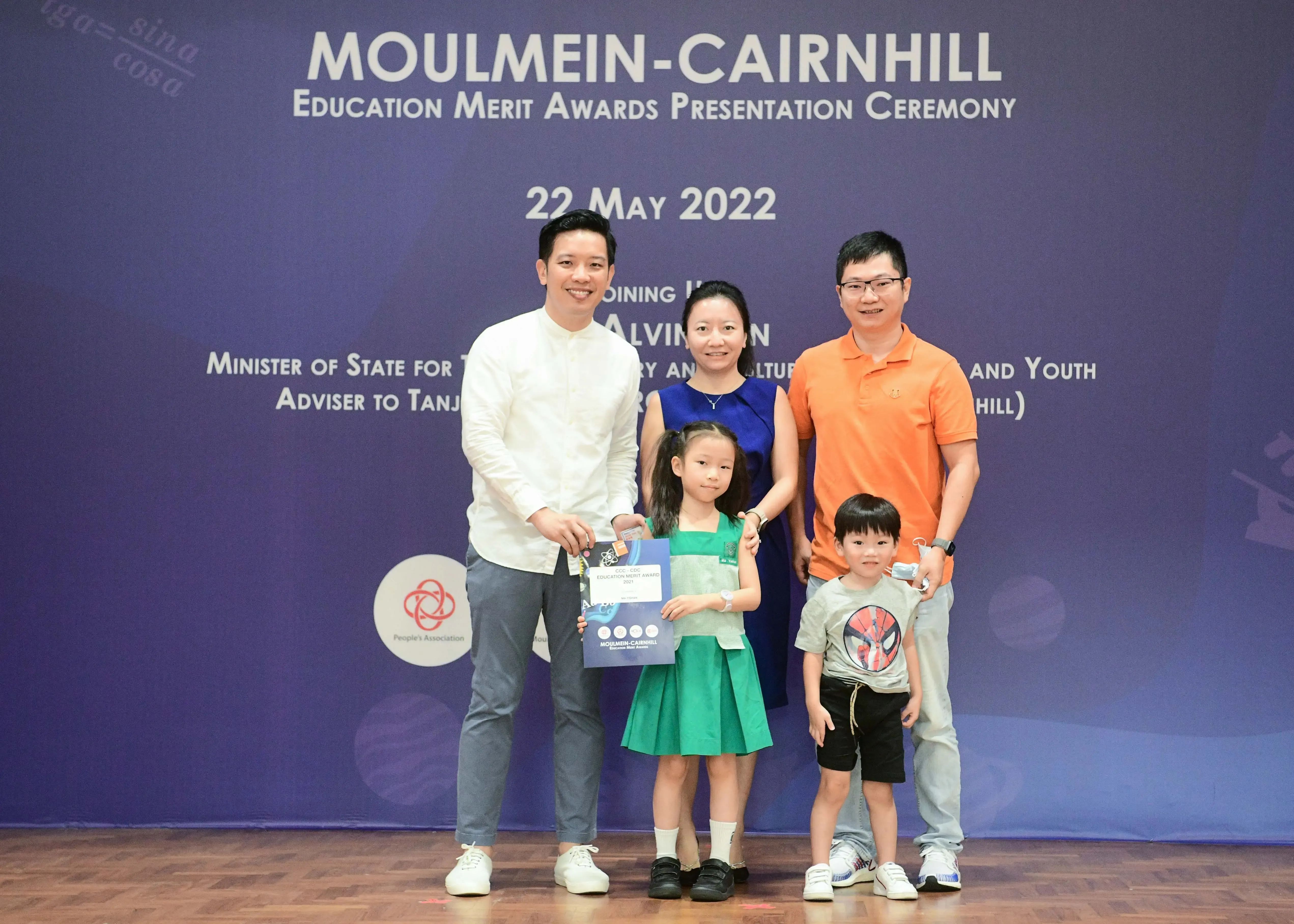 Five people pose at the Moulmein-Cairnhill Education Merit Awards Ceremony on 22 May 2022, with a girl holding a certificate.